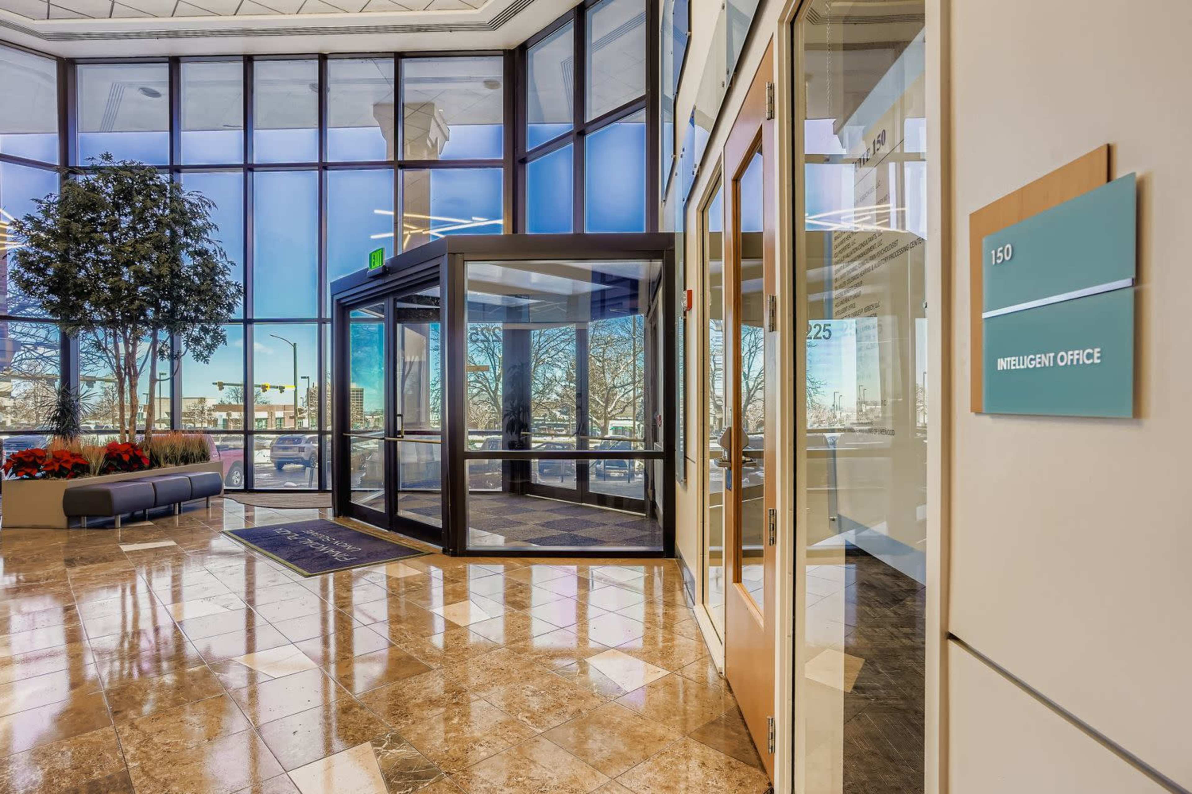 The image shows a modern office lobby with large glass windows, a revolving door, marble flooring, and a blue wall sign indicating "INTELLIGENT OFFICE."