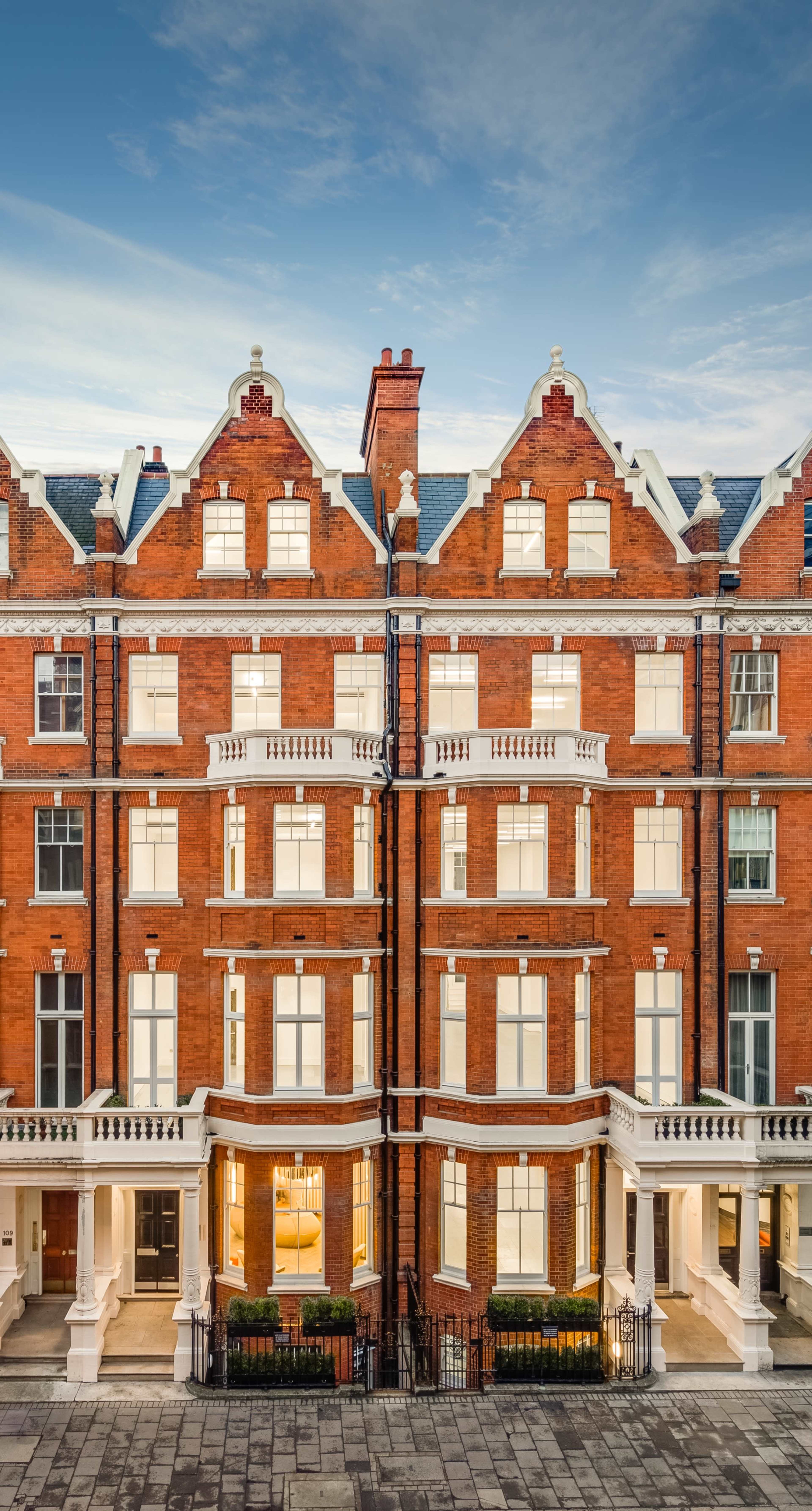 The image shows a row of red brick buildings with multiple stories, featuring large windows and decorative elements on the façade.