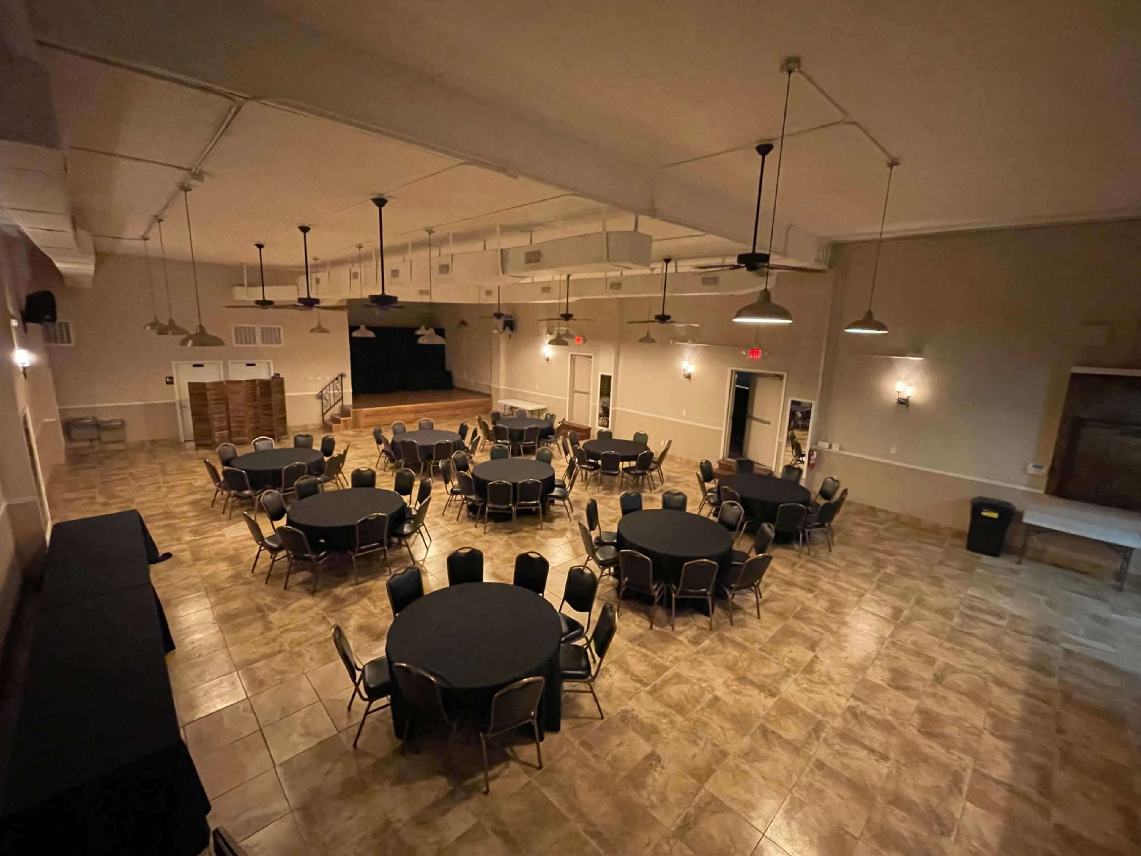 A large event space with round tables set up in rows and a stage at the far end.