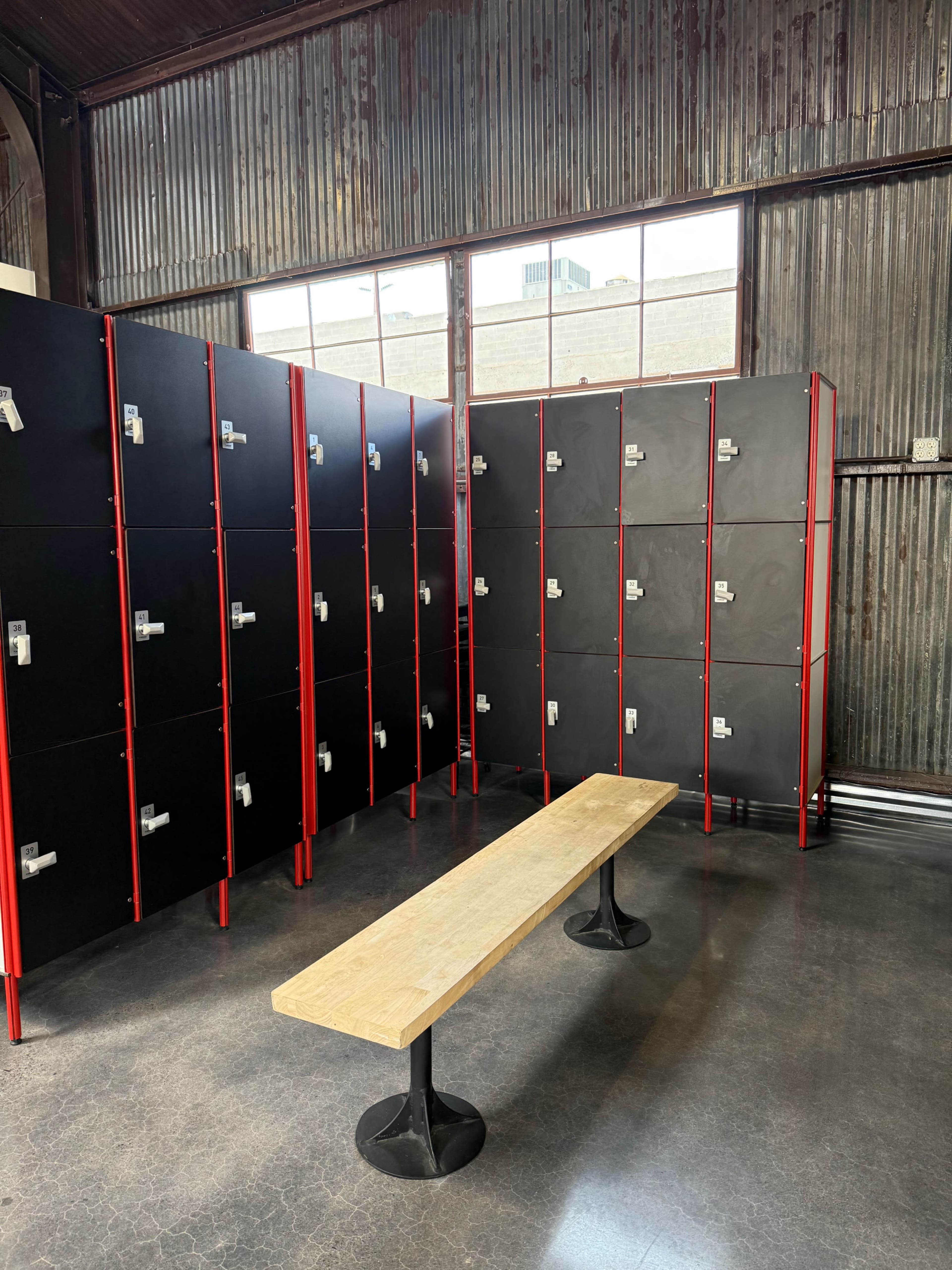 The image shows a room with several black lockers arranged against a metal wall, accompanied by a wooden bench in the center.