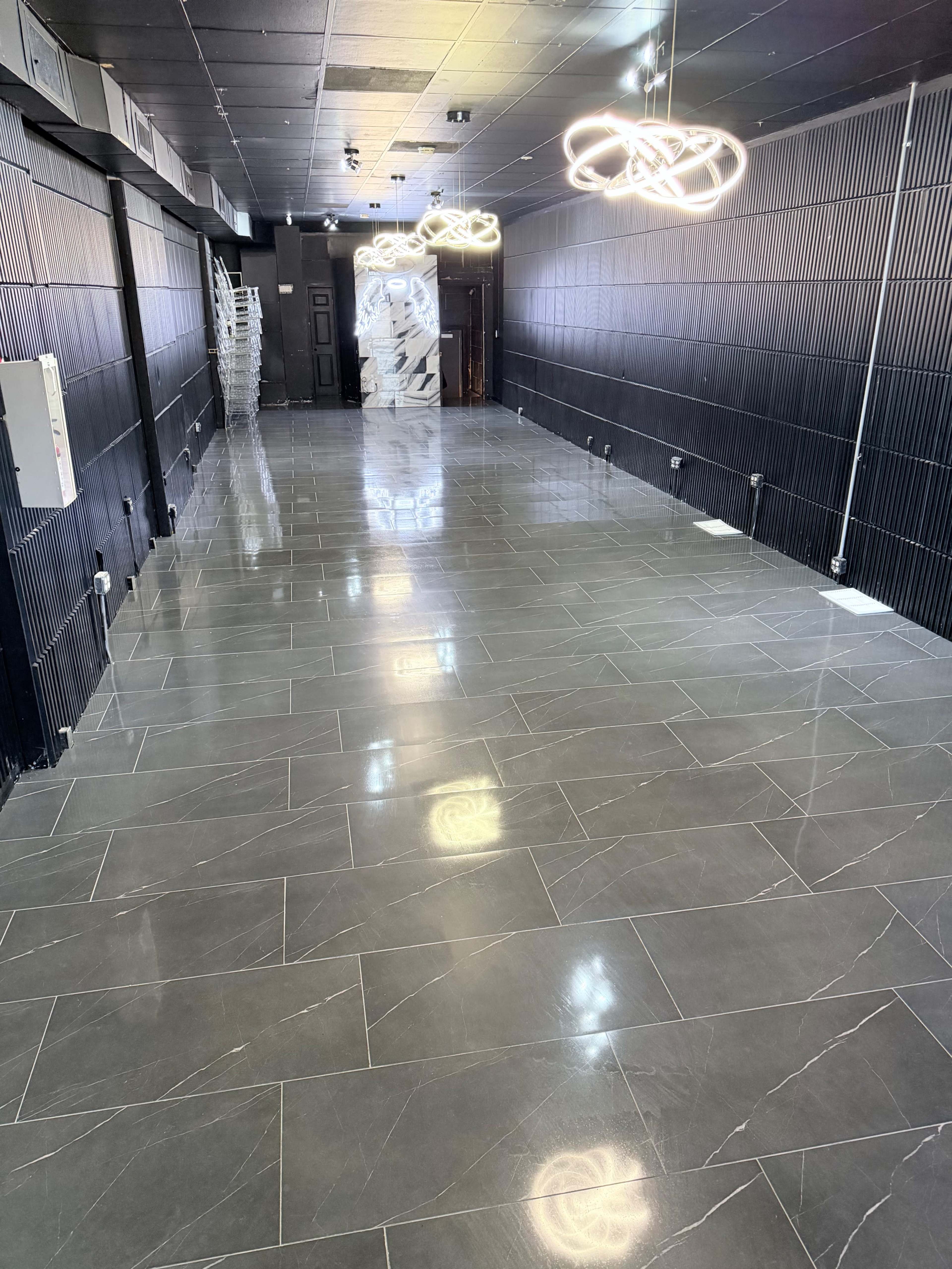 The image shows a spacious room with polished gray tile flooring, modern lighting fixtures, and black walls.
