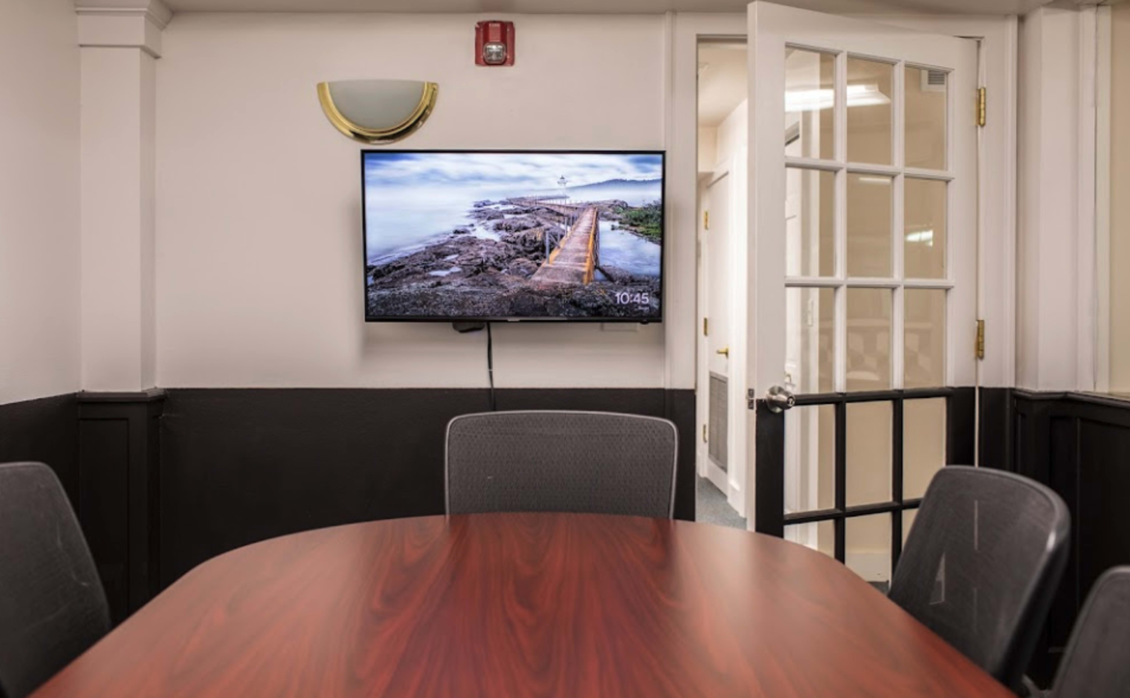 A conference room features a large wooden table and a wall-mounted television displaying a coastal landscape.