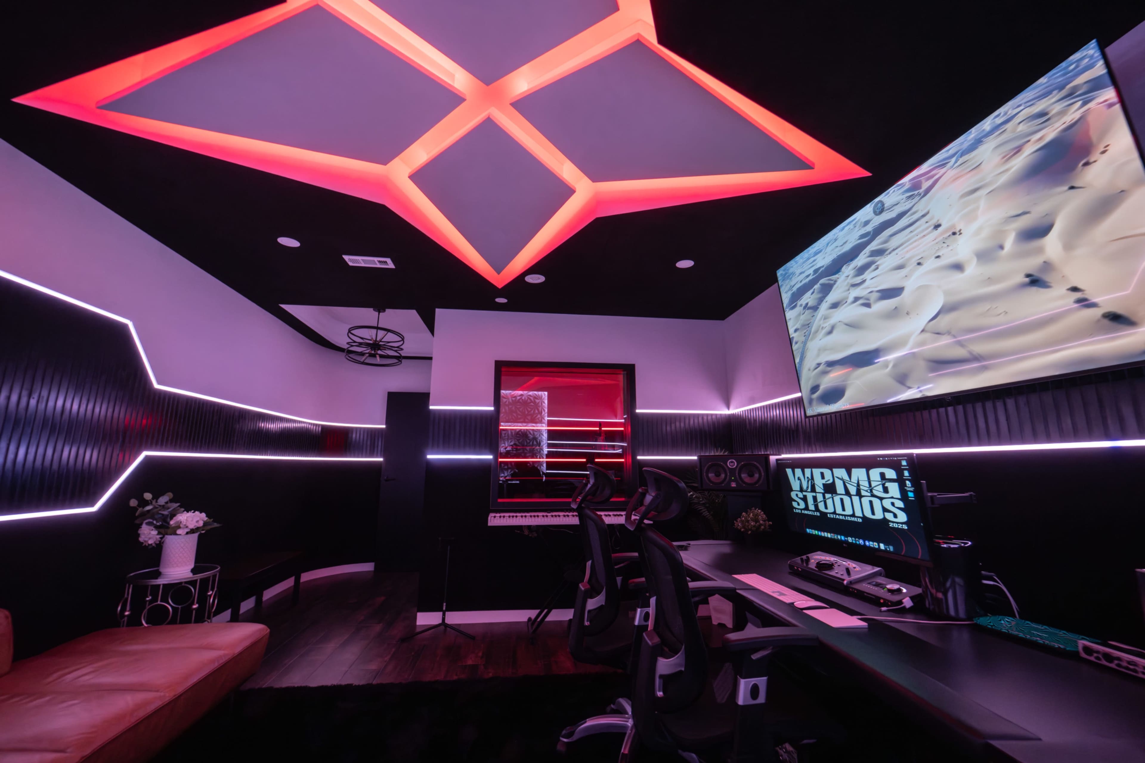 A modern recording studio featuring a sleek design with LED lighting, sound equipment, and a large screen displaying visuals.