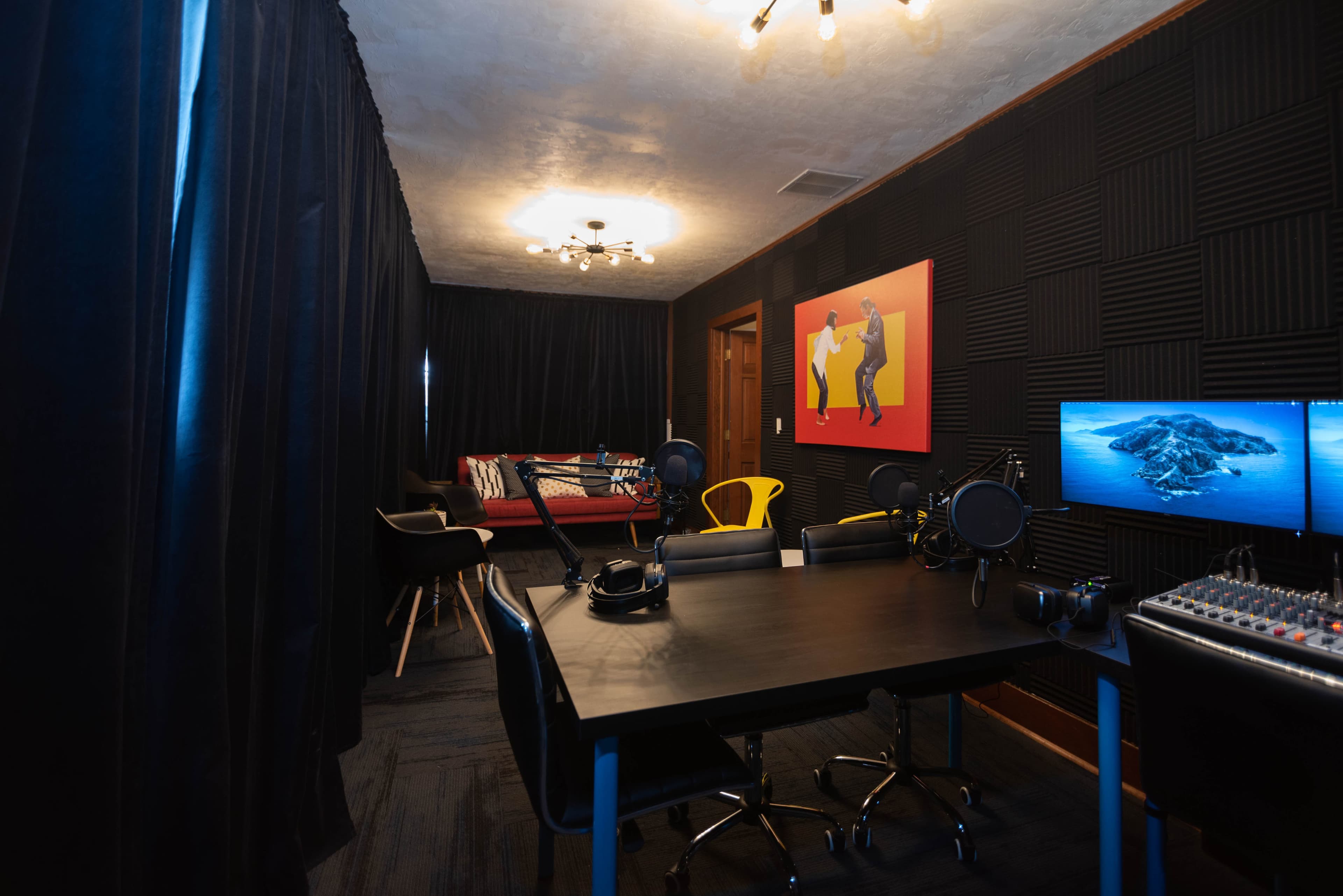 The image shows a soundproof recording studio featuring a desk with microphones, headphones, and a sound mixer, alongside seating and vibrant wall art.