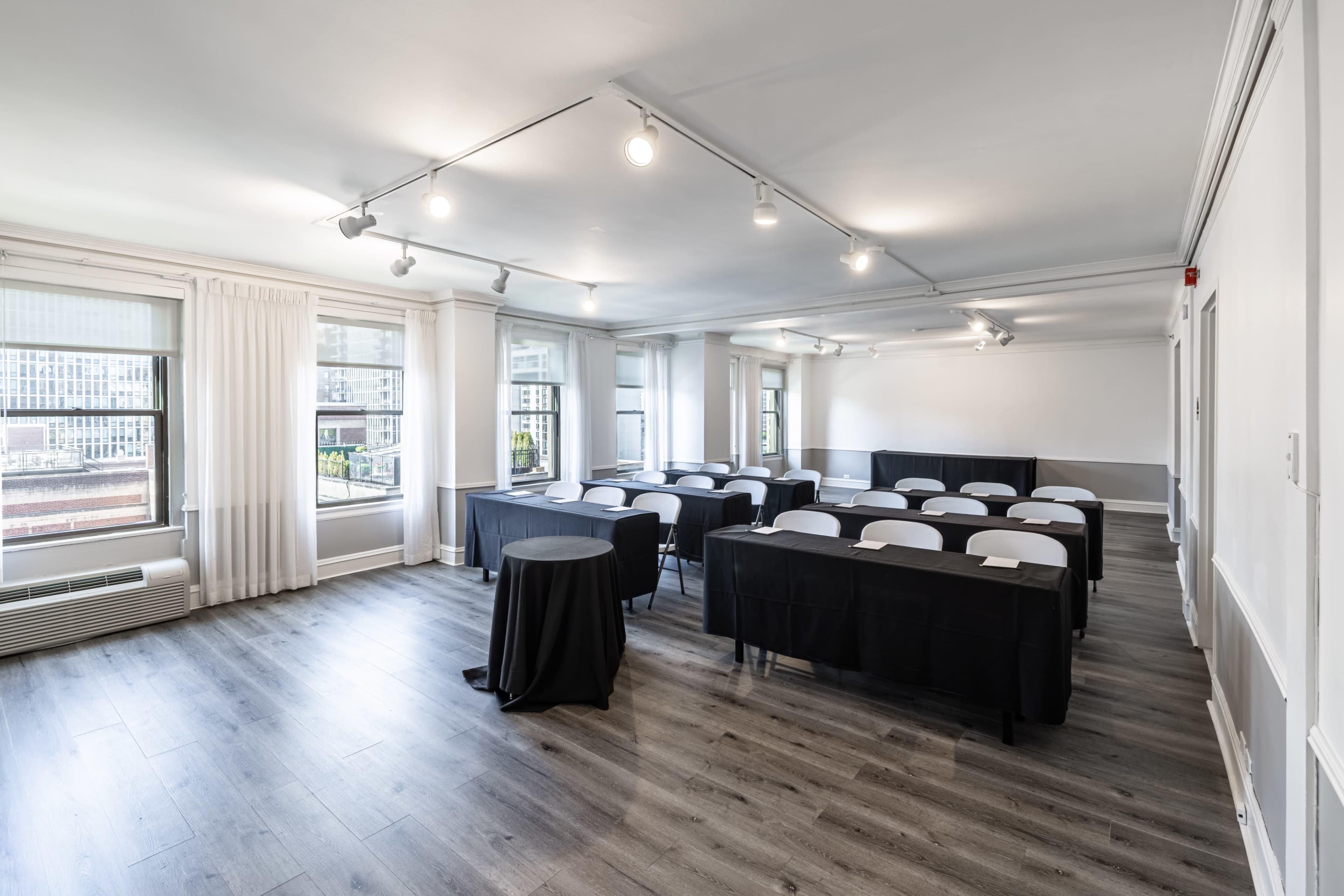 The image shows a modern conference room equipped with rows of tables and chairs, large windows, and contemporary lighting.