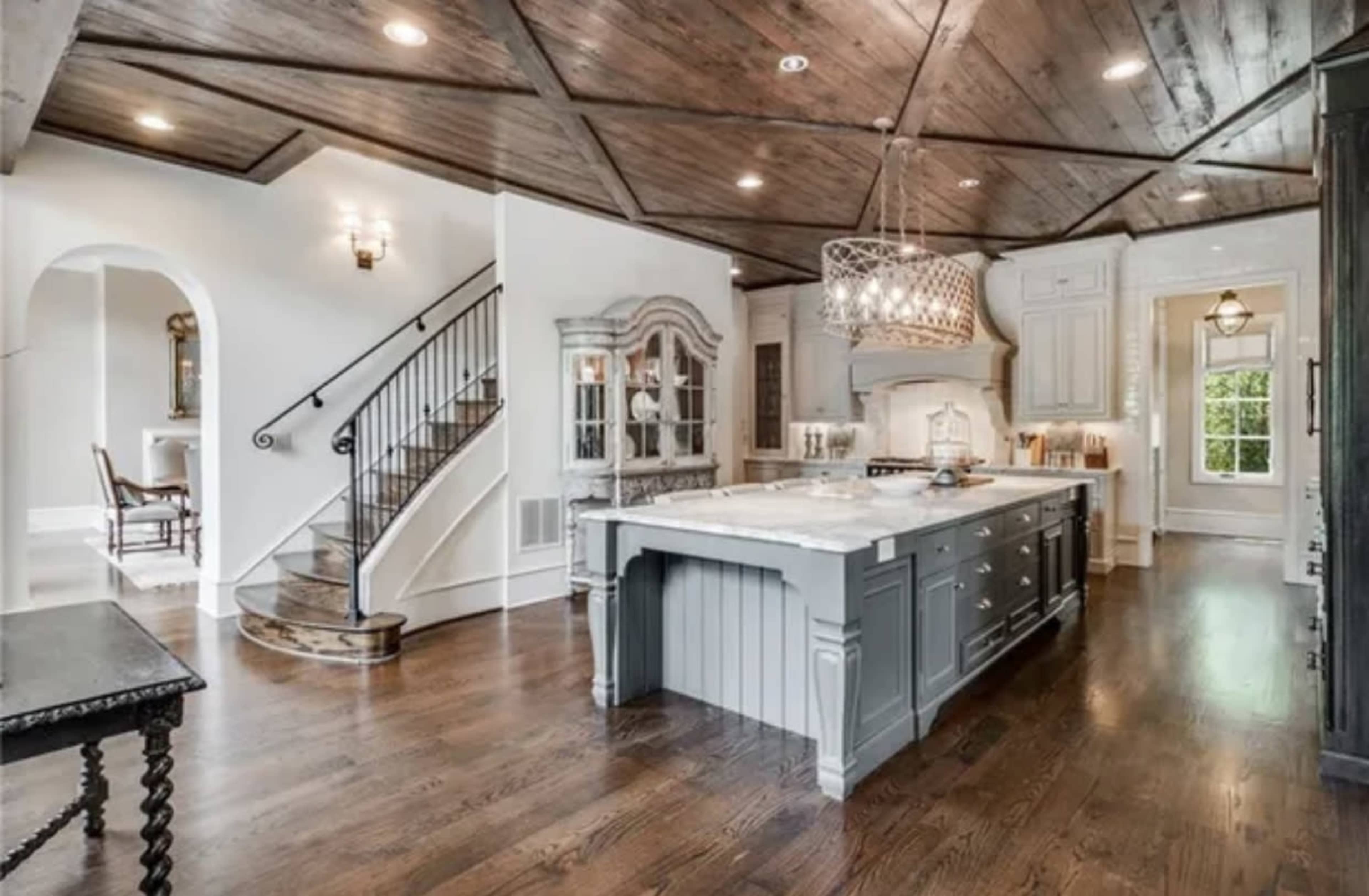 A spacious kitchen featuring a large central island, wood-paneled ceiling, and elegant cabinetry.