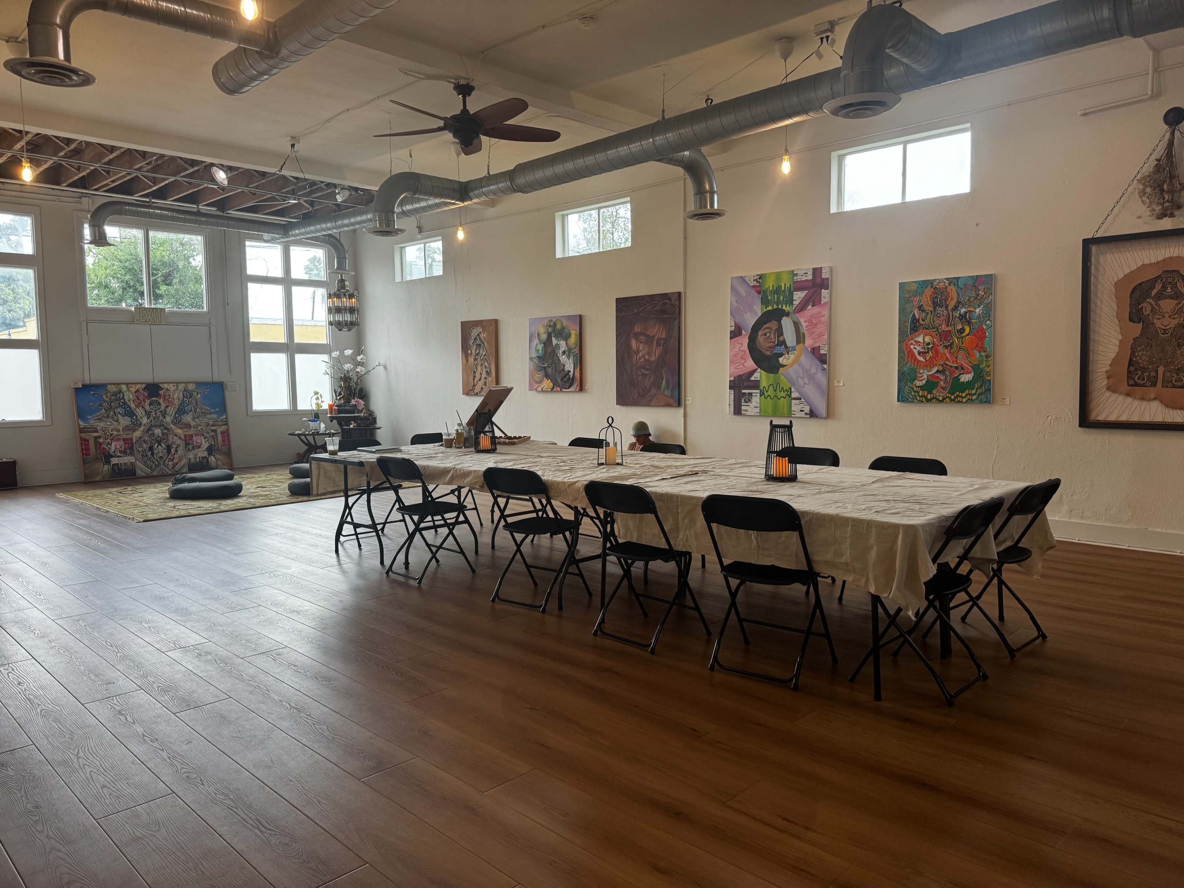 The image shows a spacious room with a long table set for a gathering, surrounded by chairs, and adorned with various pieces of art on the walls.