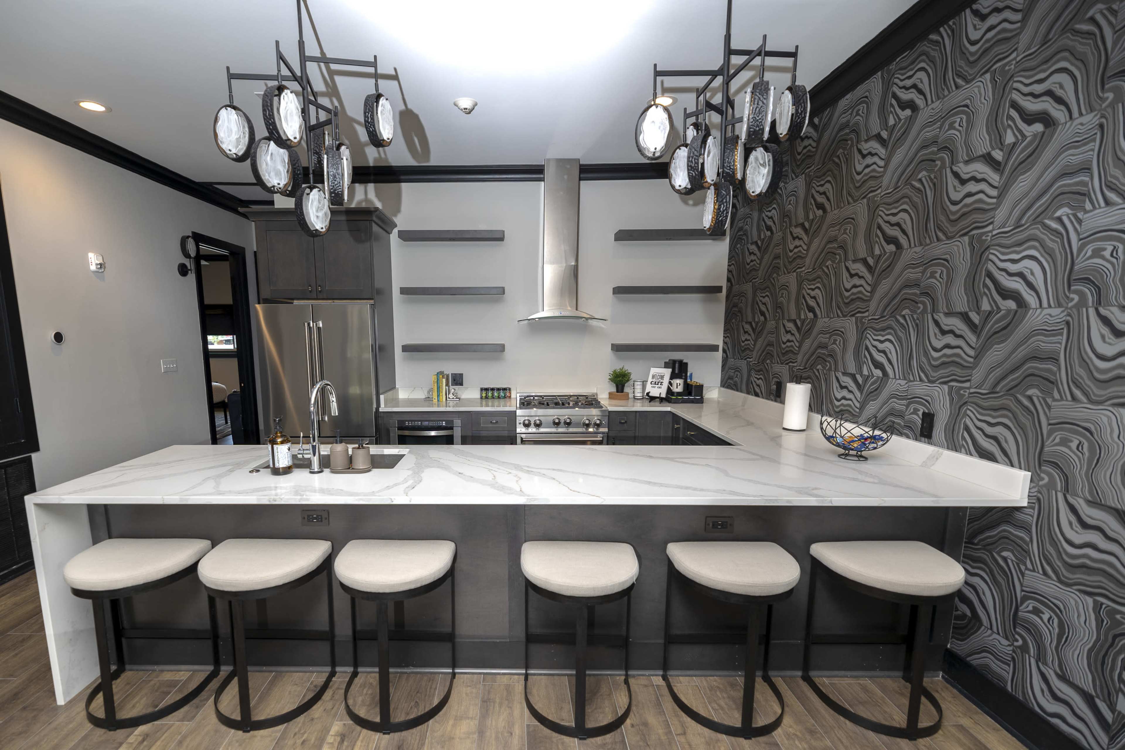 The image shows a modern kitchen with a marble countertop island, six bar stools, and decorative pendant lights above.