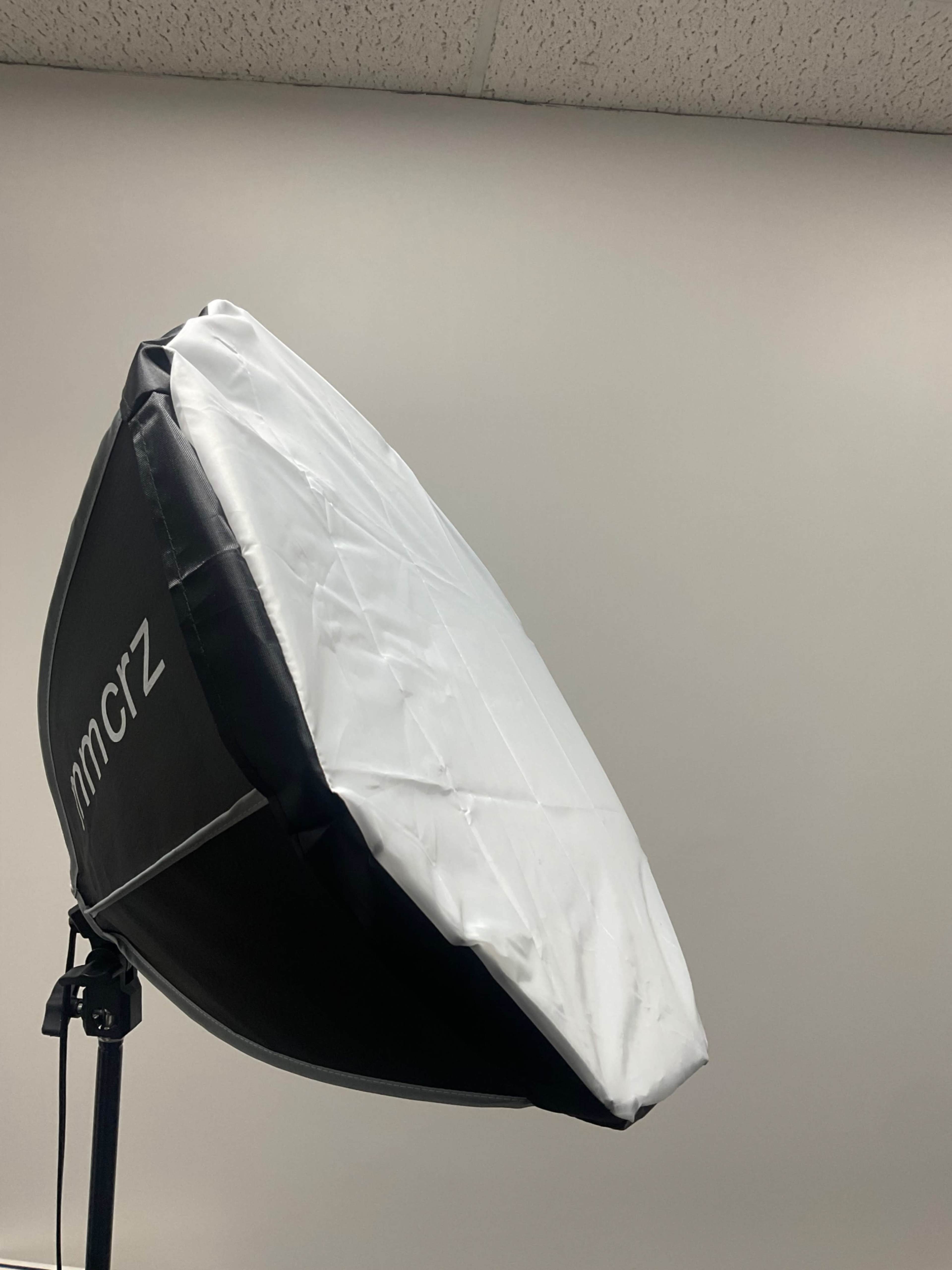 A softbox light is set up on a stand against a plain gray wall.