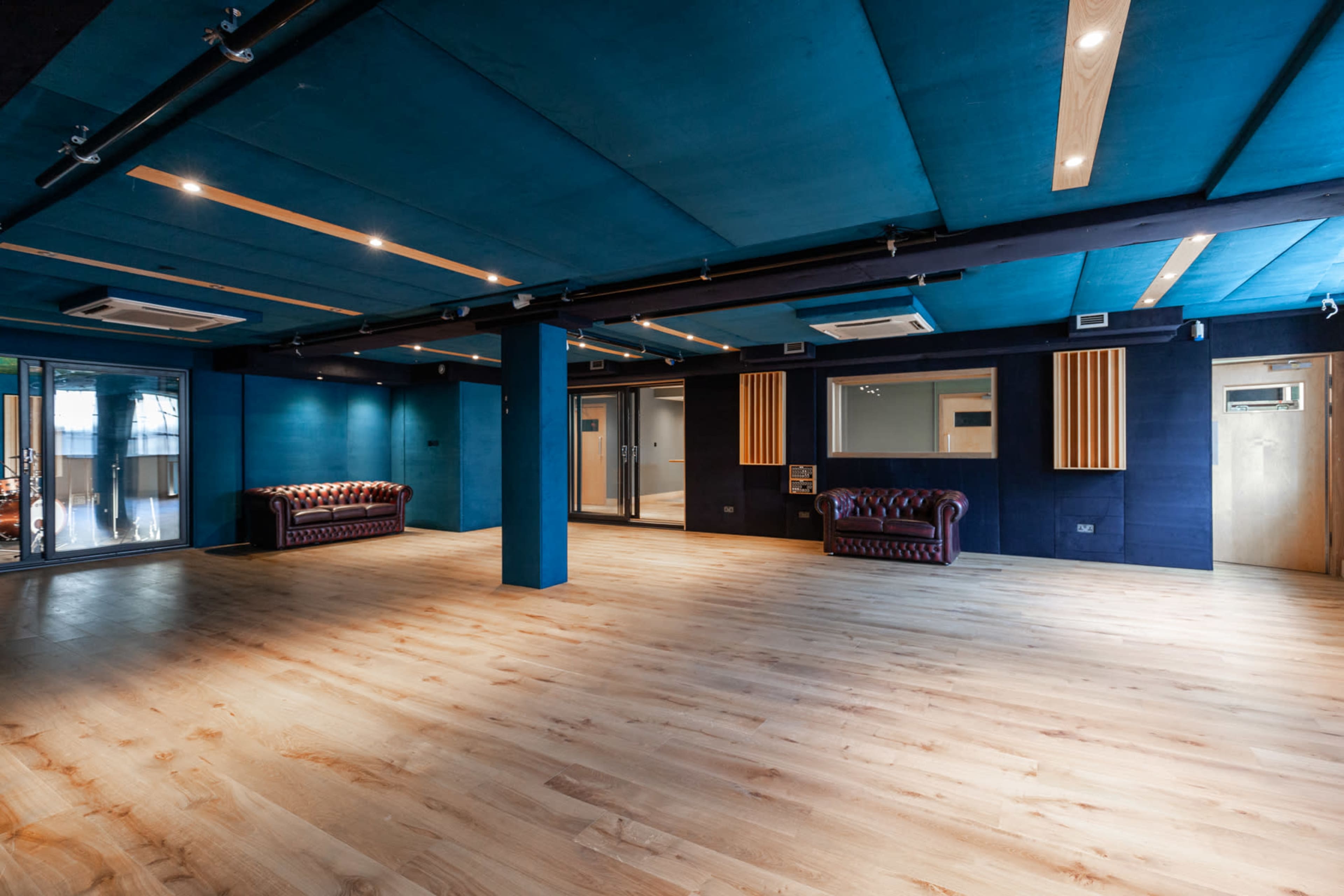 A spacious room with dark blue walls and a wooden floor, featuring two leather sofas and doors on the sides.