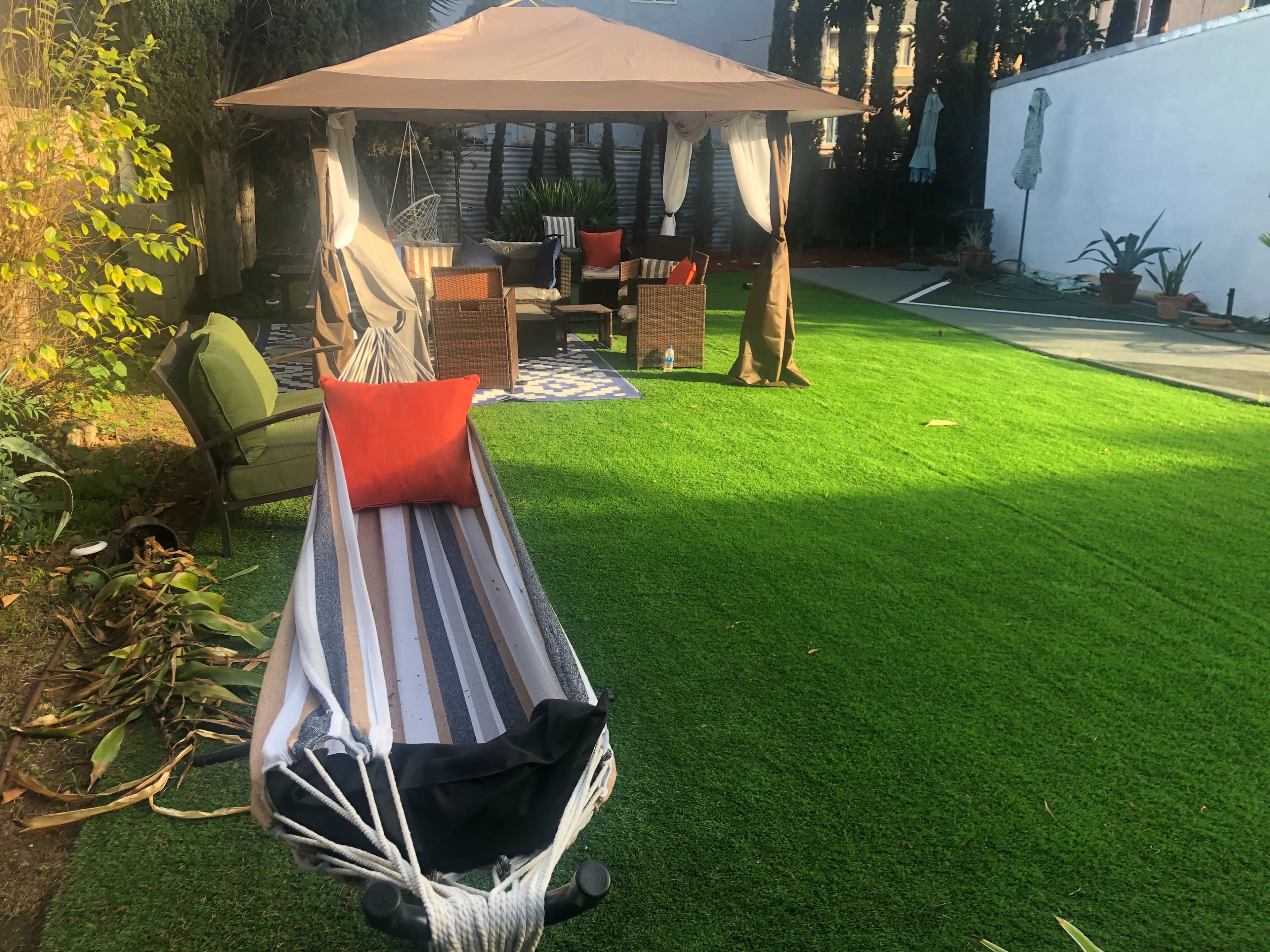 A backyard with a hammock, a shaded seating area under a canopy, and green artificial grass.
