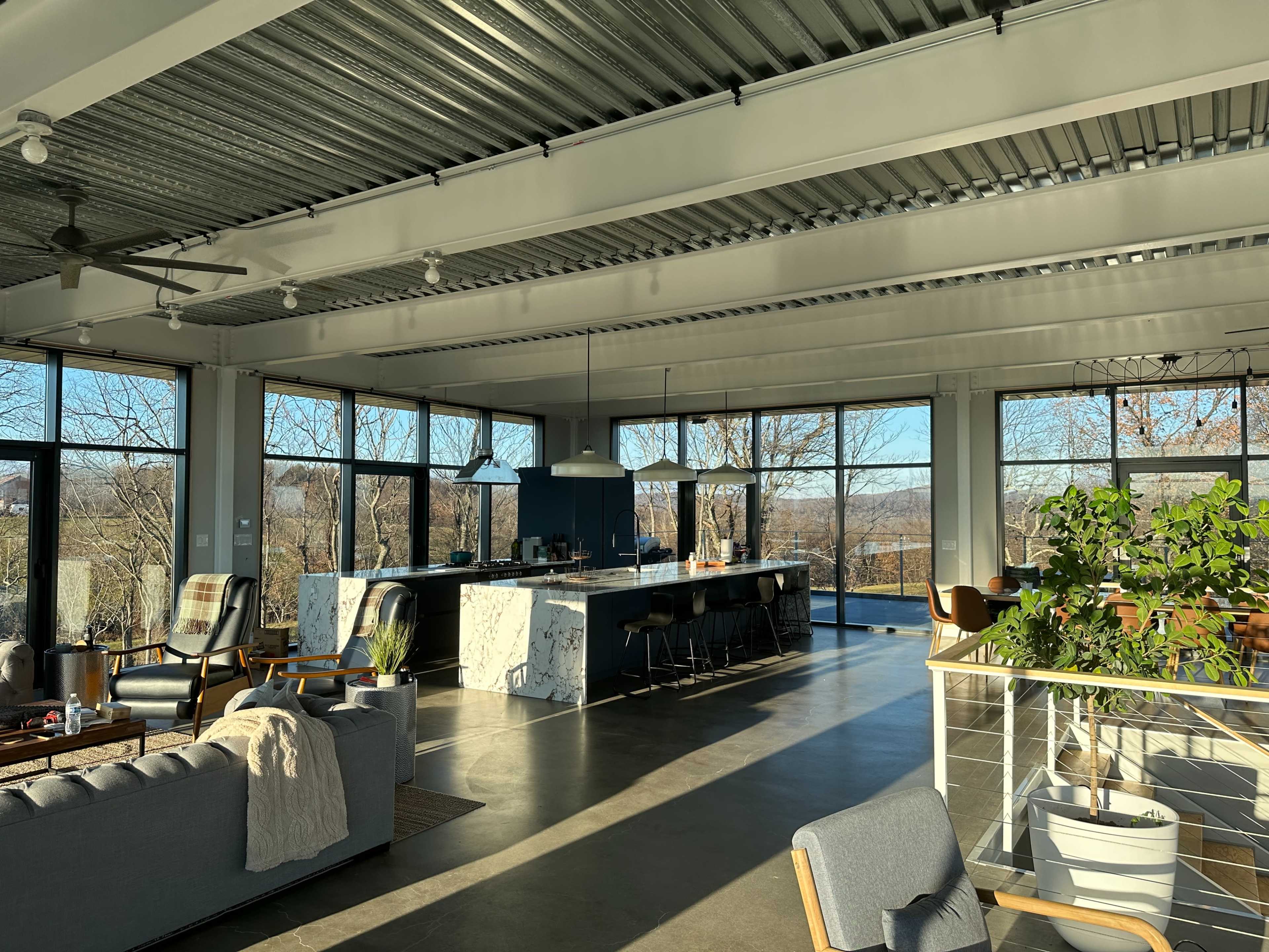 A modern, open-concept living space with large windows, a kitchen island, and various seating arrangements.