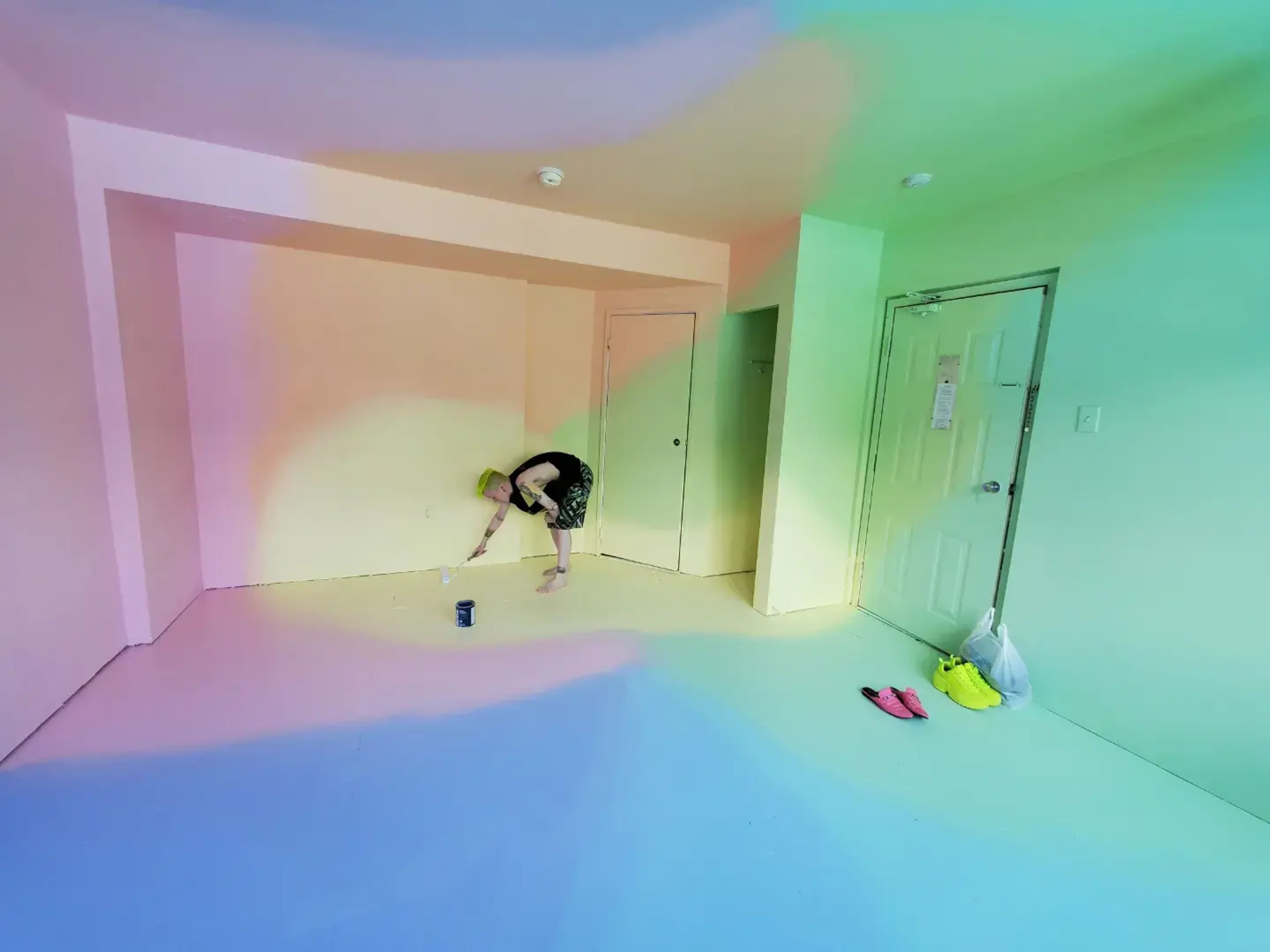 A person is painting the walls of a brightly colored room with gradient shades of pastel hues.