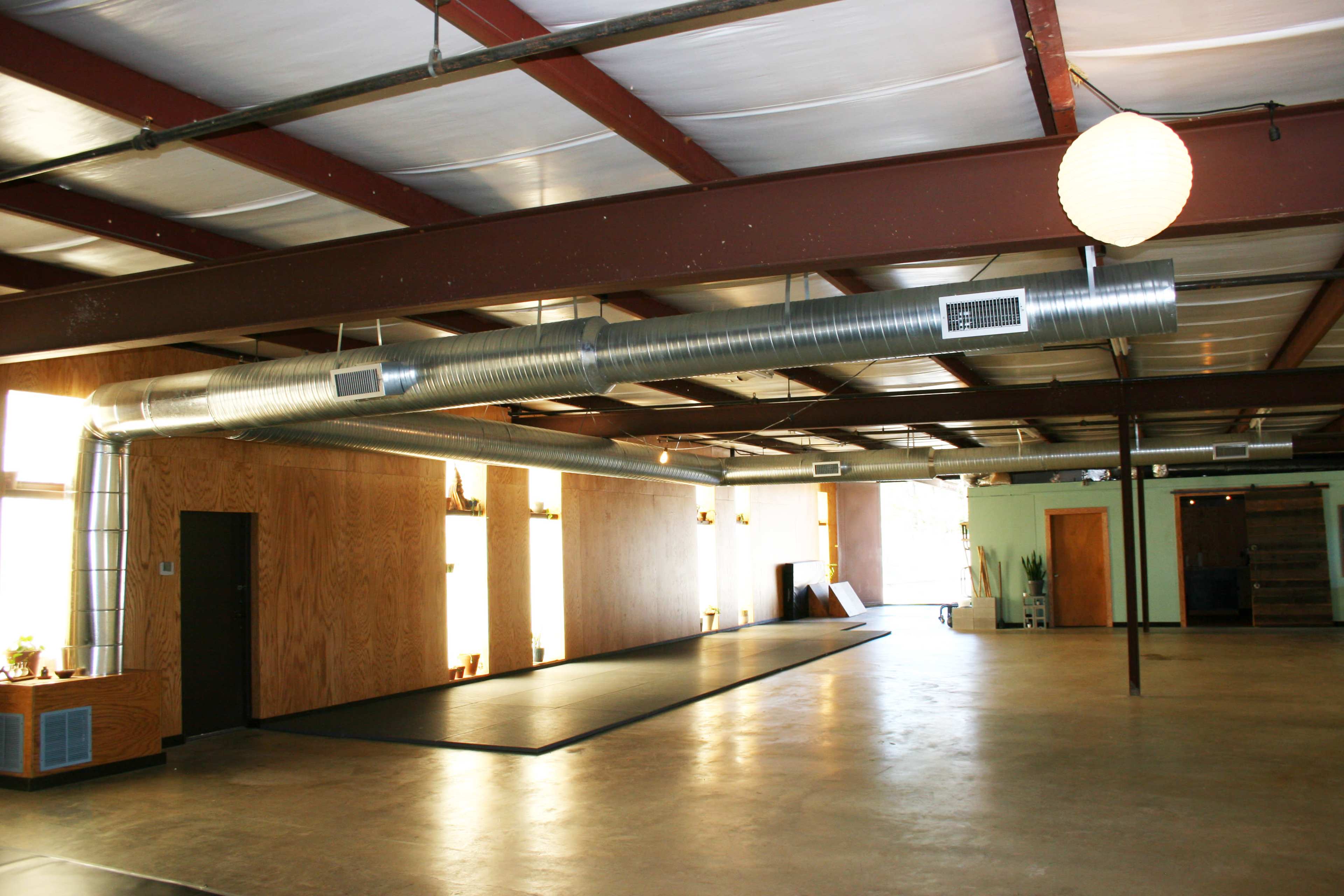 An open interior space with concrete floors, wooden walls, and a large metal duct running along the ceiling.