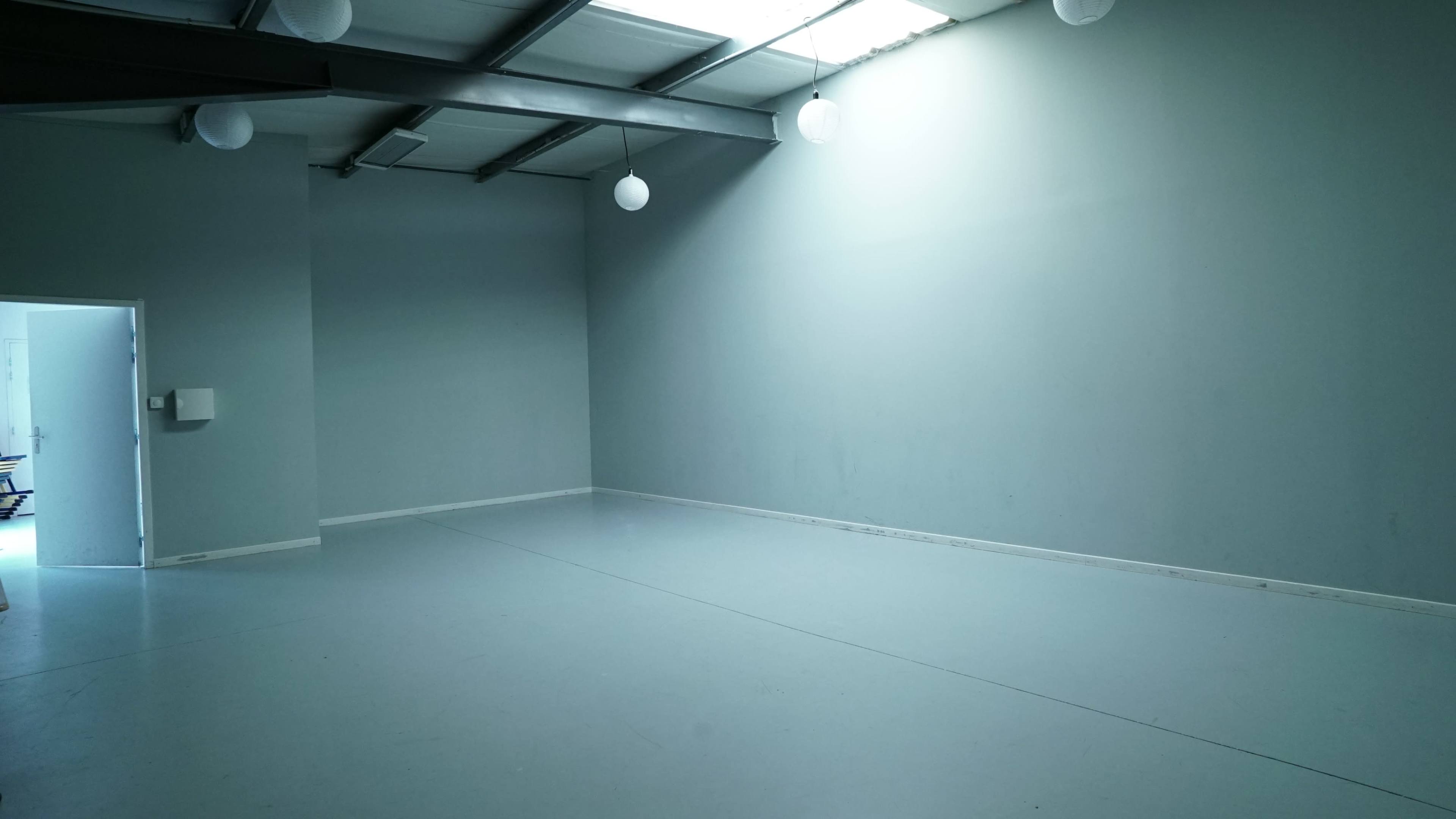 An empty room with a gray wall, concrete floor, and overhead light fixtures.