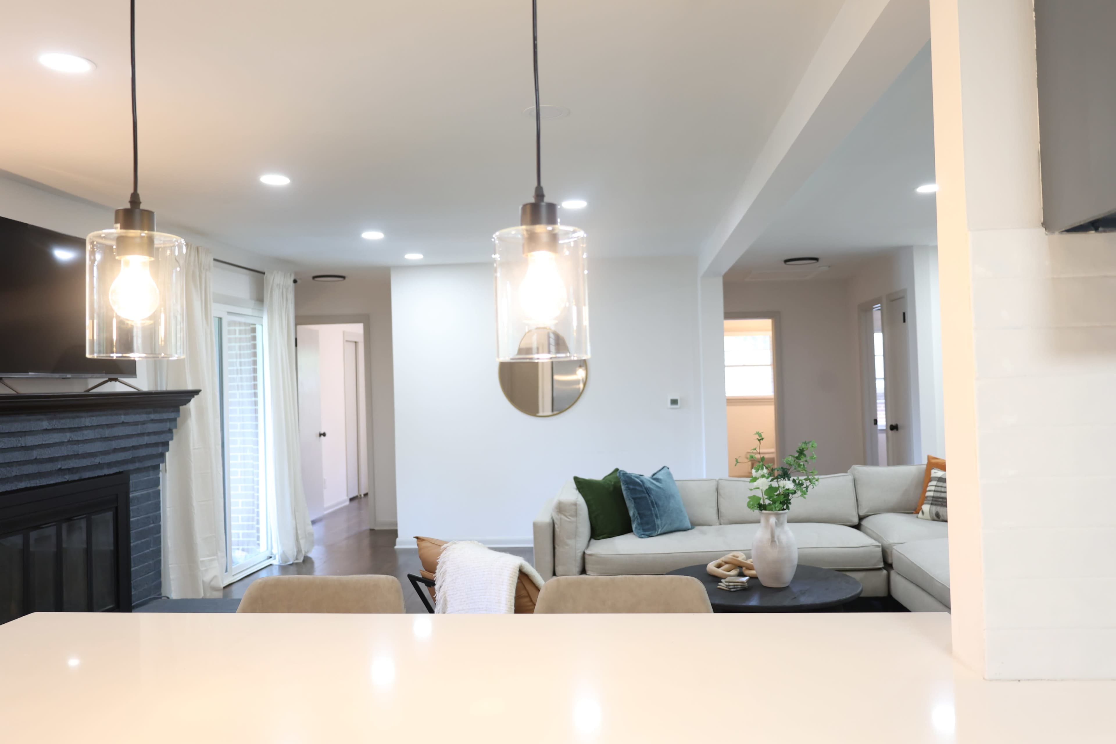 A modern living space with a light-colored sectional sofa, a coffee table, and two pendant lights hanging over a kitchen island.