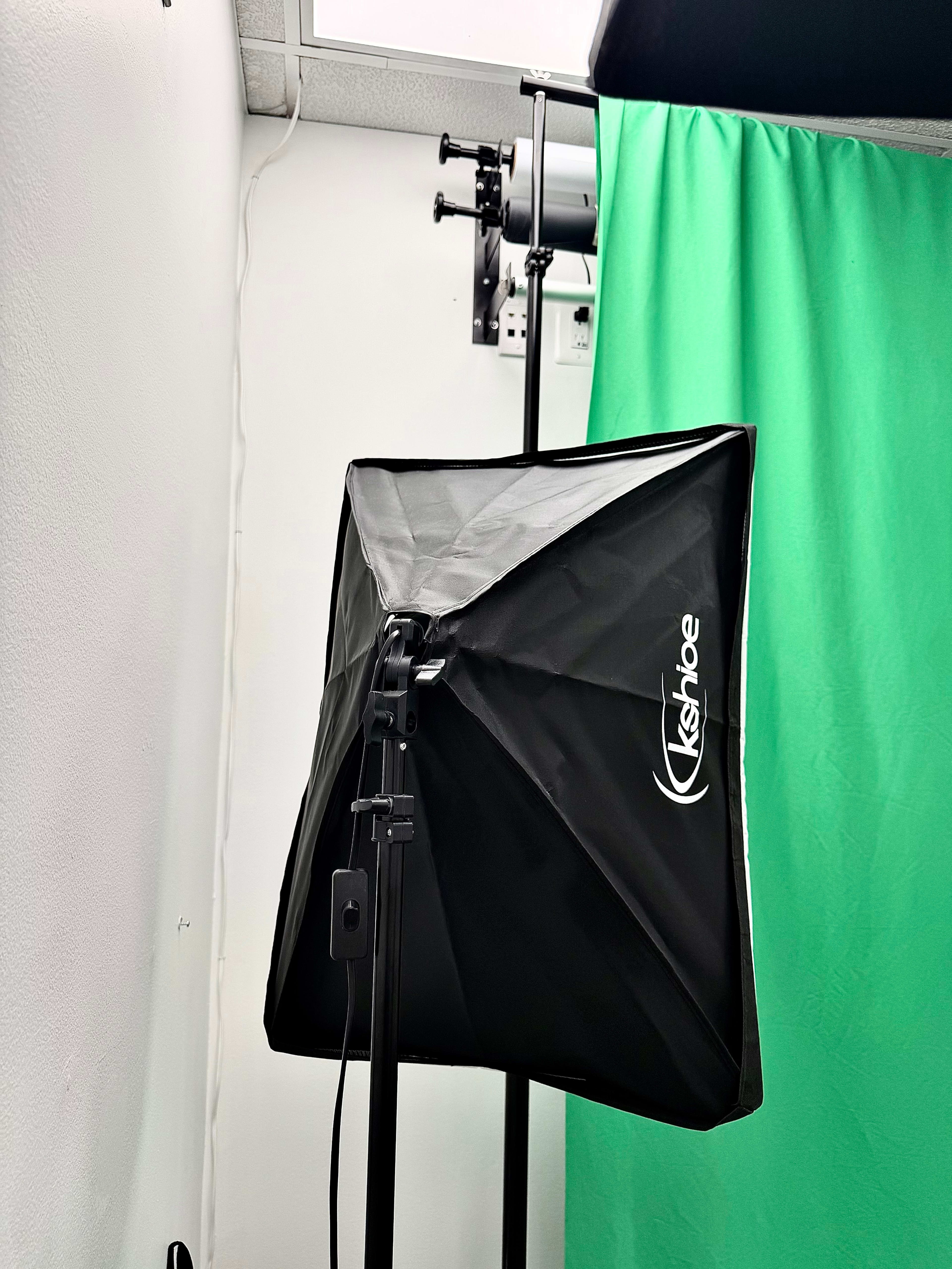 The image shows a black softbox light positioned next to a green backdrop in a photography setup.