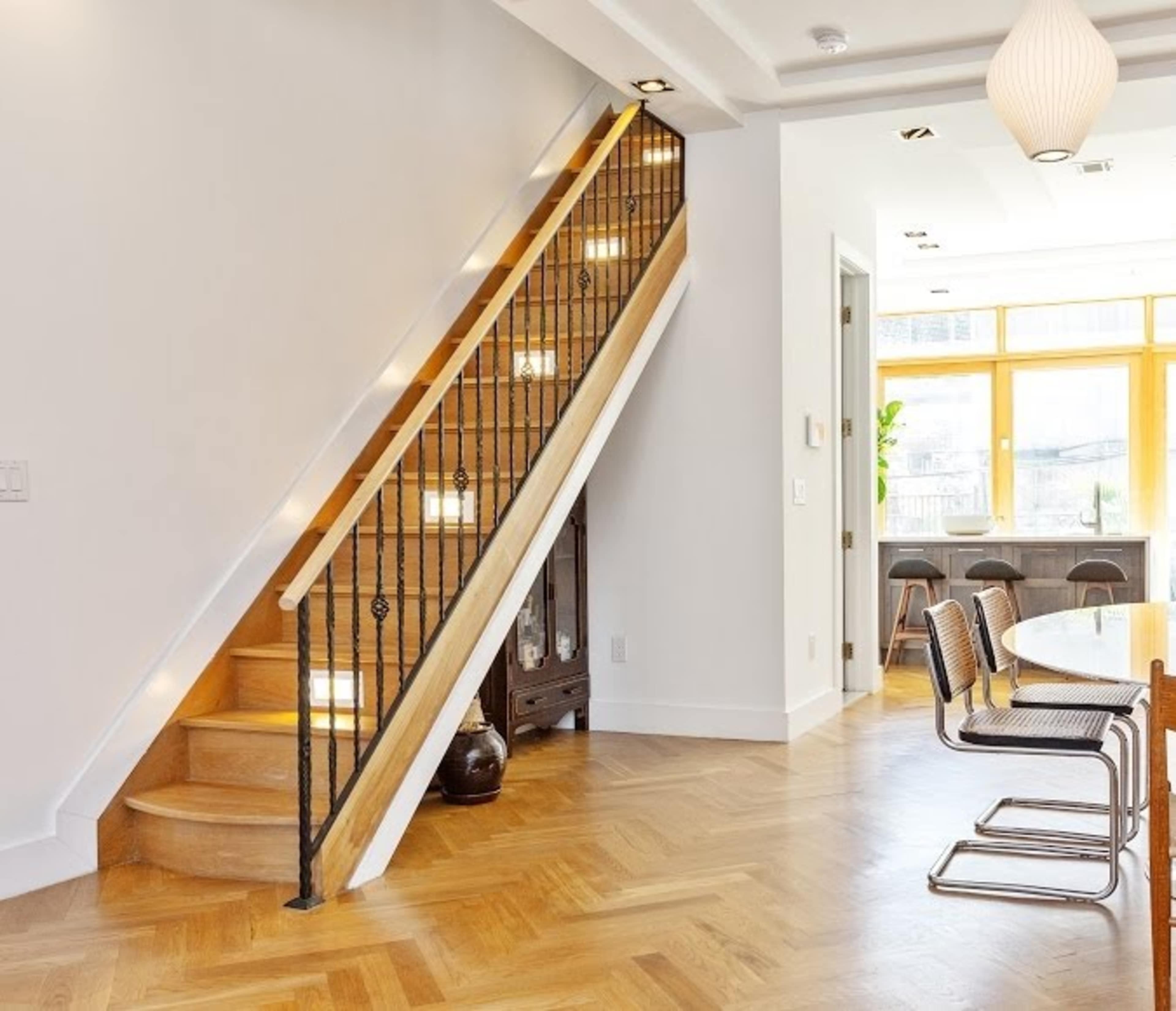A modern stairway with wooden steps and a black railing leads to an upper level in a bright, open space featuring a dining area.