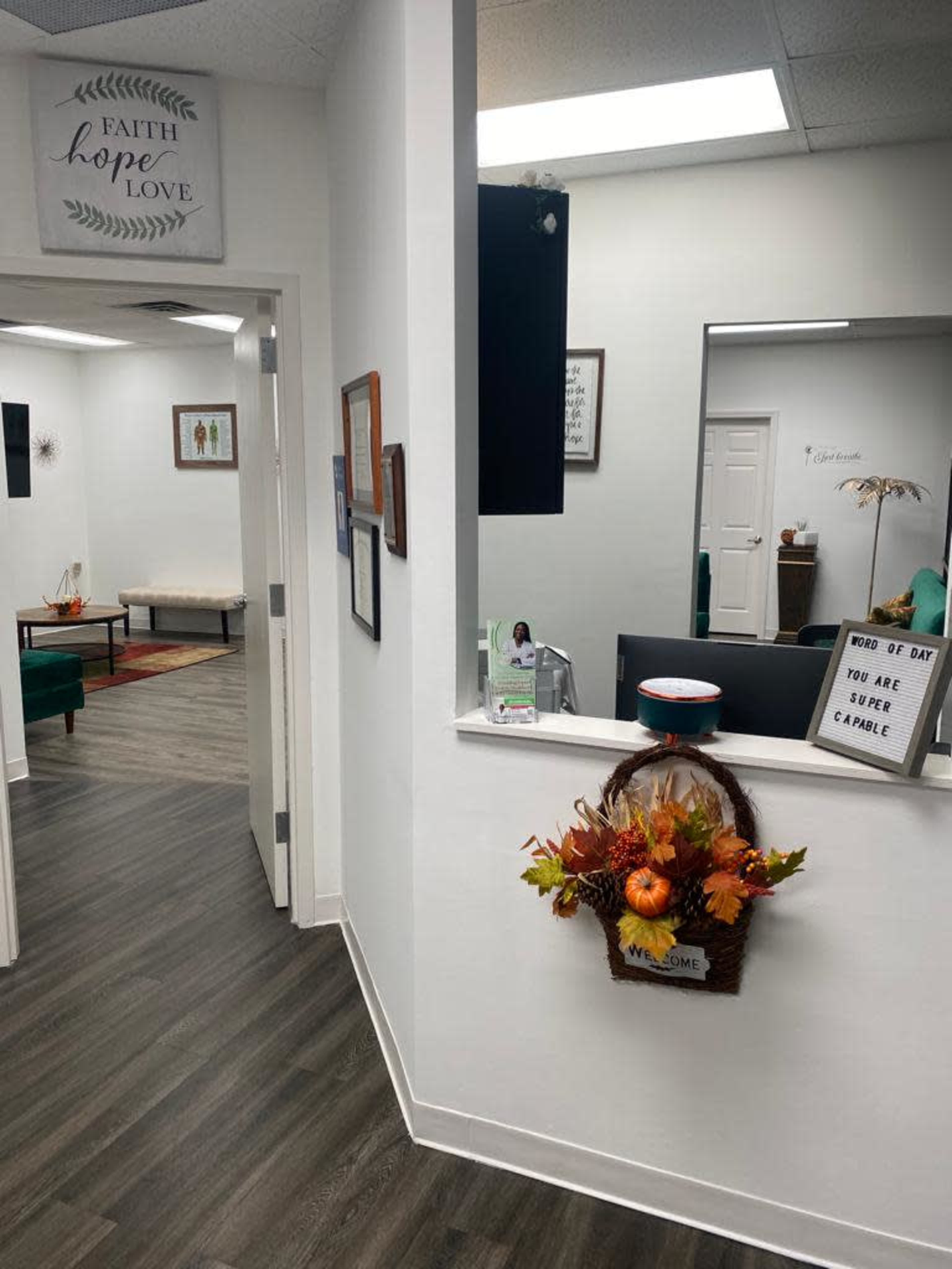 A bright hallway with framed artwork and a decorative basket of autumn leaves leads to a waiting area featuring green furniture.