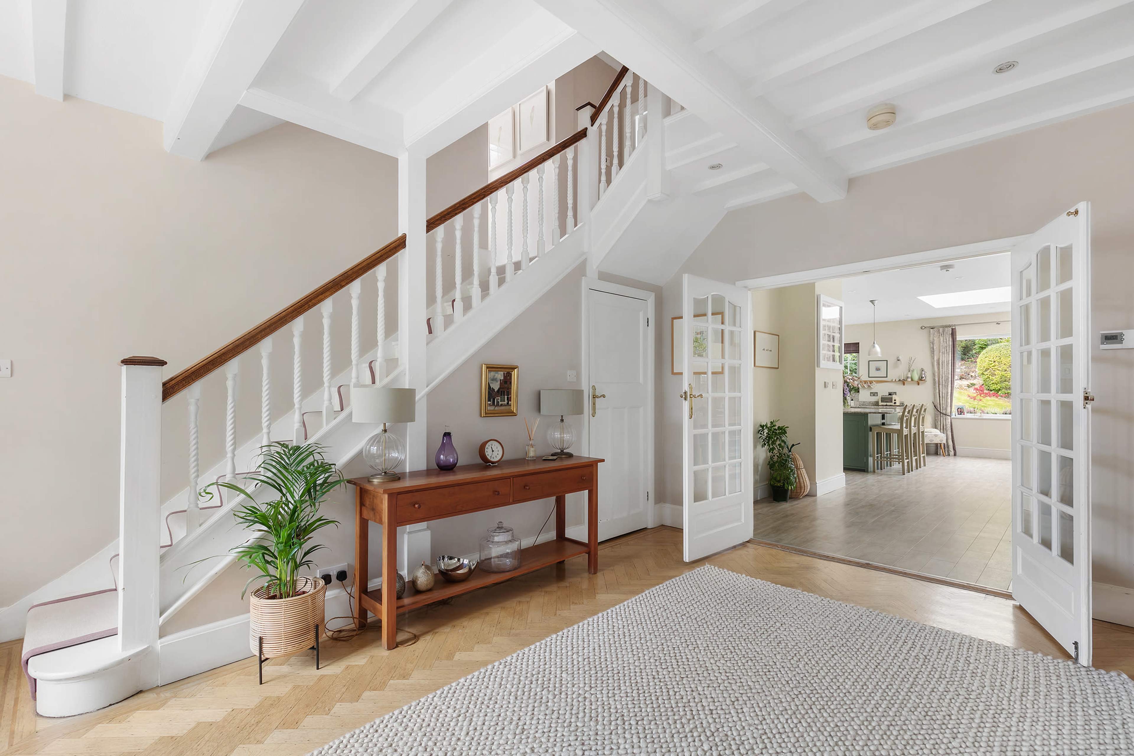 A well-lit entryway featuring a staircase, a console table with decorative items, and an open entrance to a living space visible in the background.