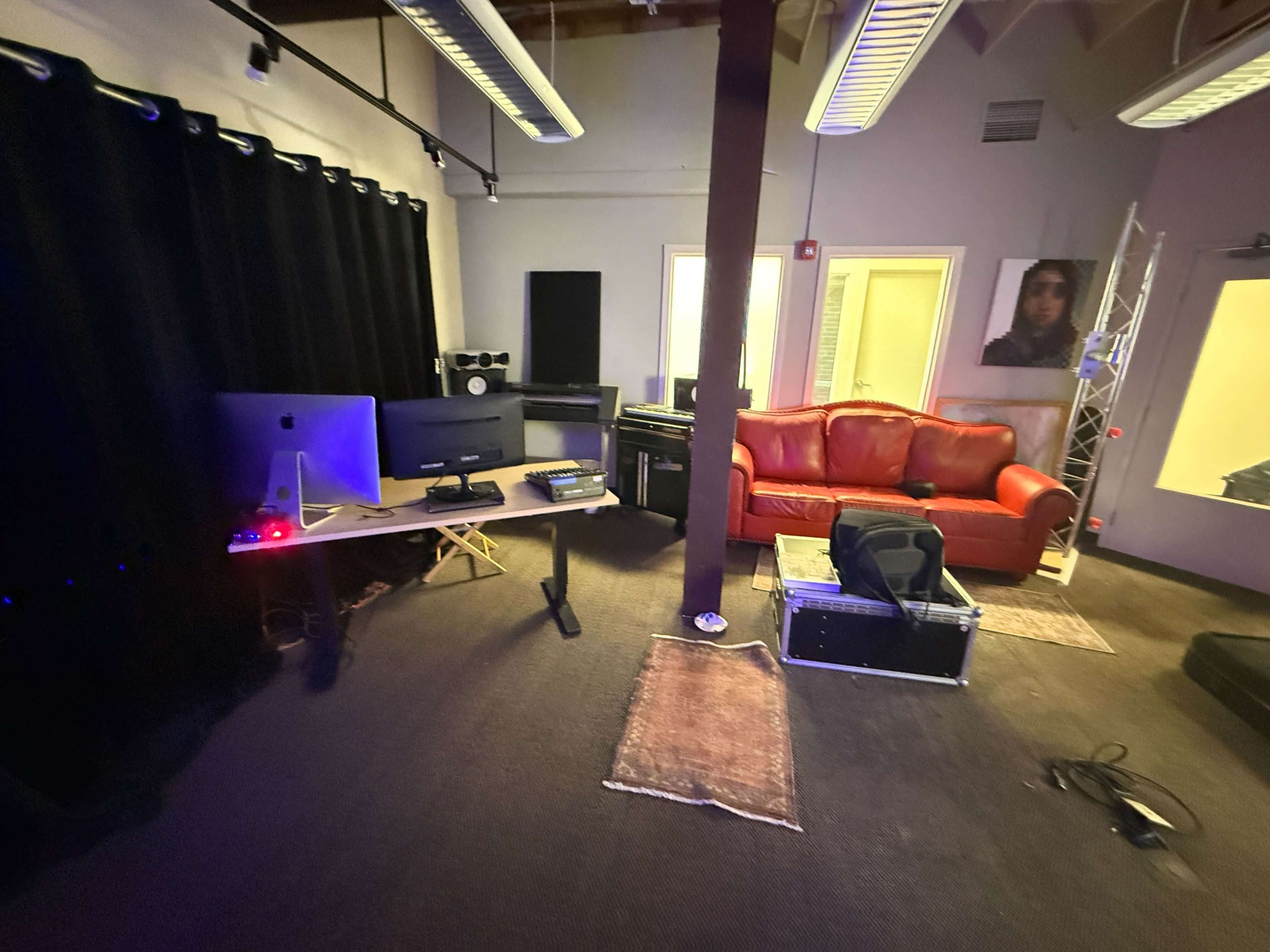 The image shows a music recording studio featuring a red couch, computers, and various audio equipment, with black curtains and a purple light.