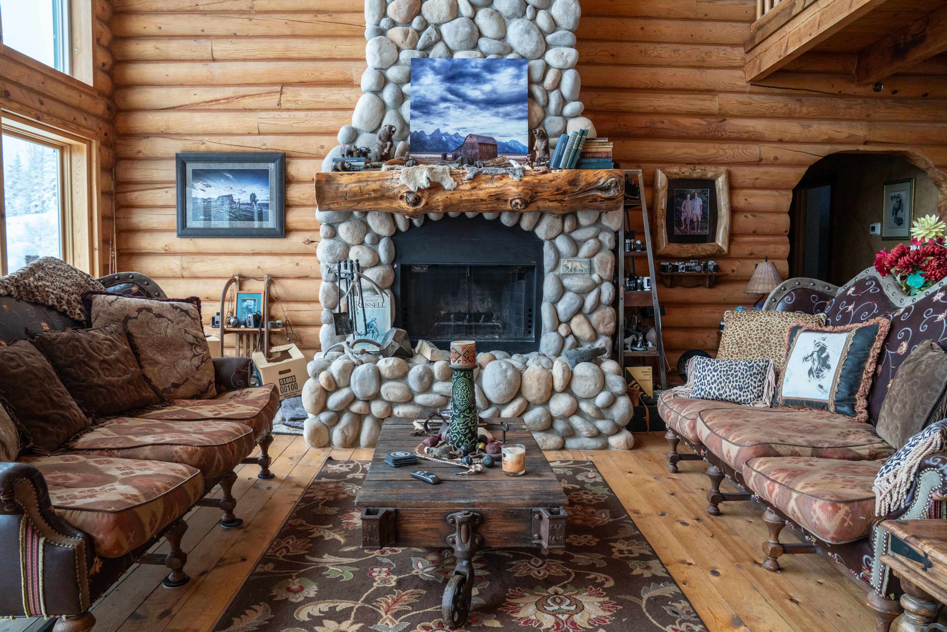 A log cabin living room with a stone fireplace, wooden furniture, and a coffee table in the center.