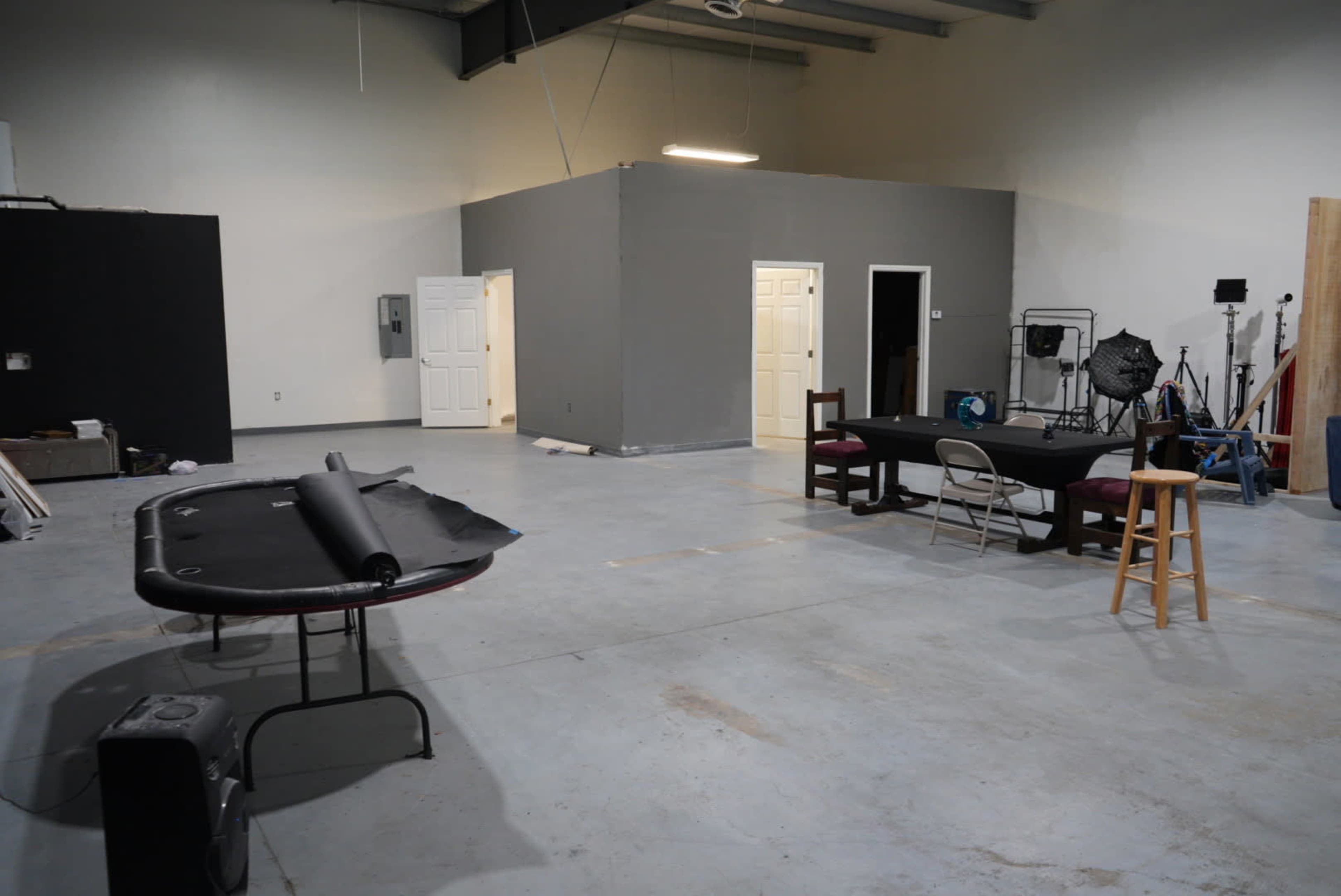 The image shows an empty studio space with gray walls, a table, chairs, and a room divider in the background.