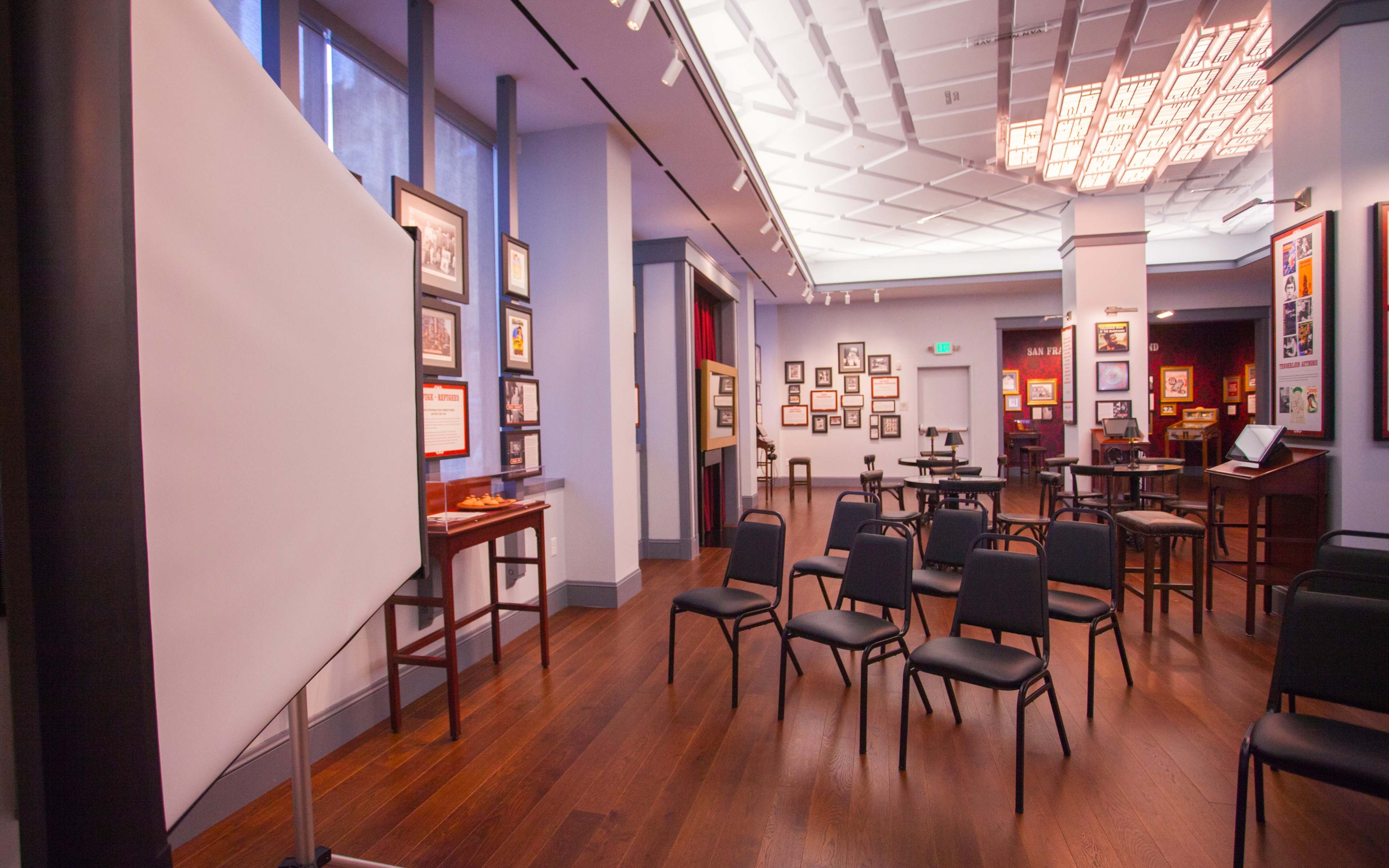 A meeting room set up with rows of black chairs facing a blank presentation board, surrounded by framed artwork on the walls.