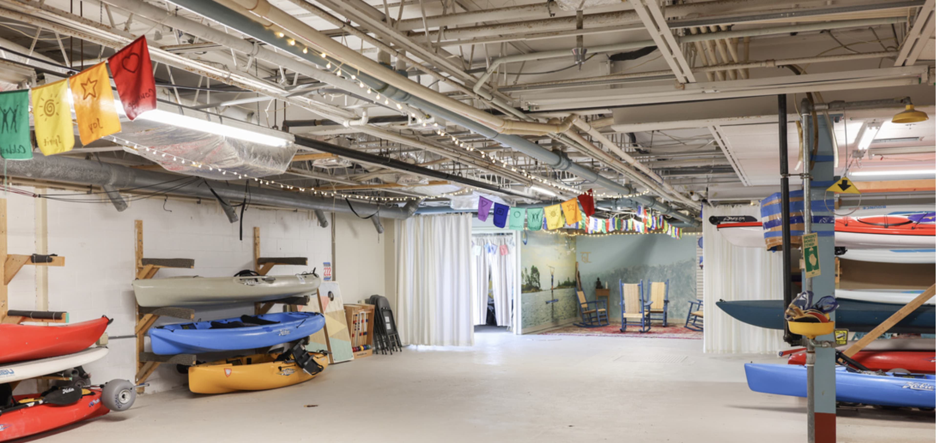 A spacious indoor area features several kayaks stacked along the walls and colorful banners hanging from the ceiling.