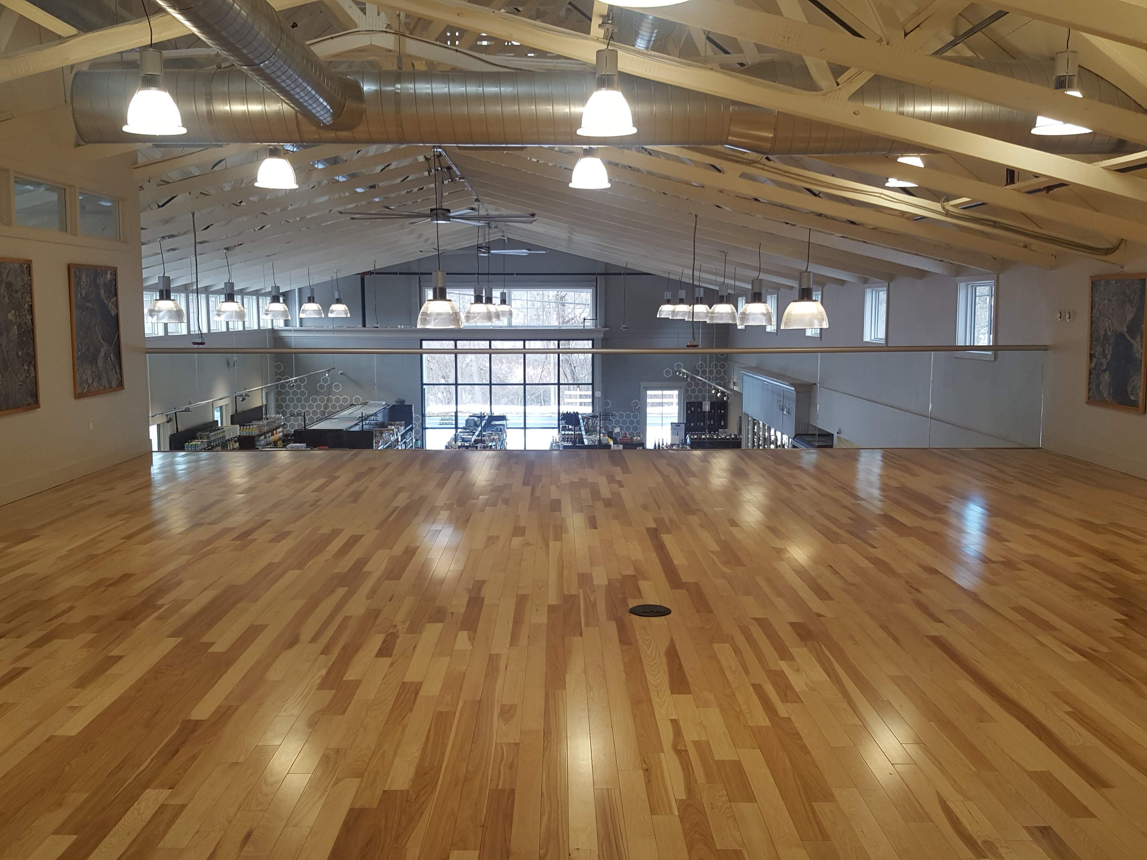 A spacious wooden floor area with large windows and industrial-style lighting in a building with exposed beams.
