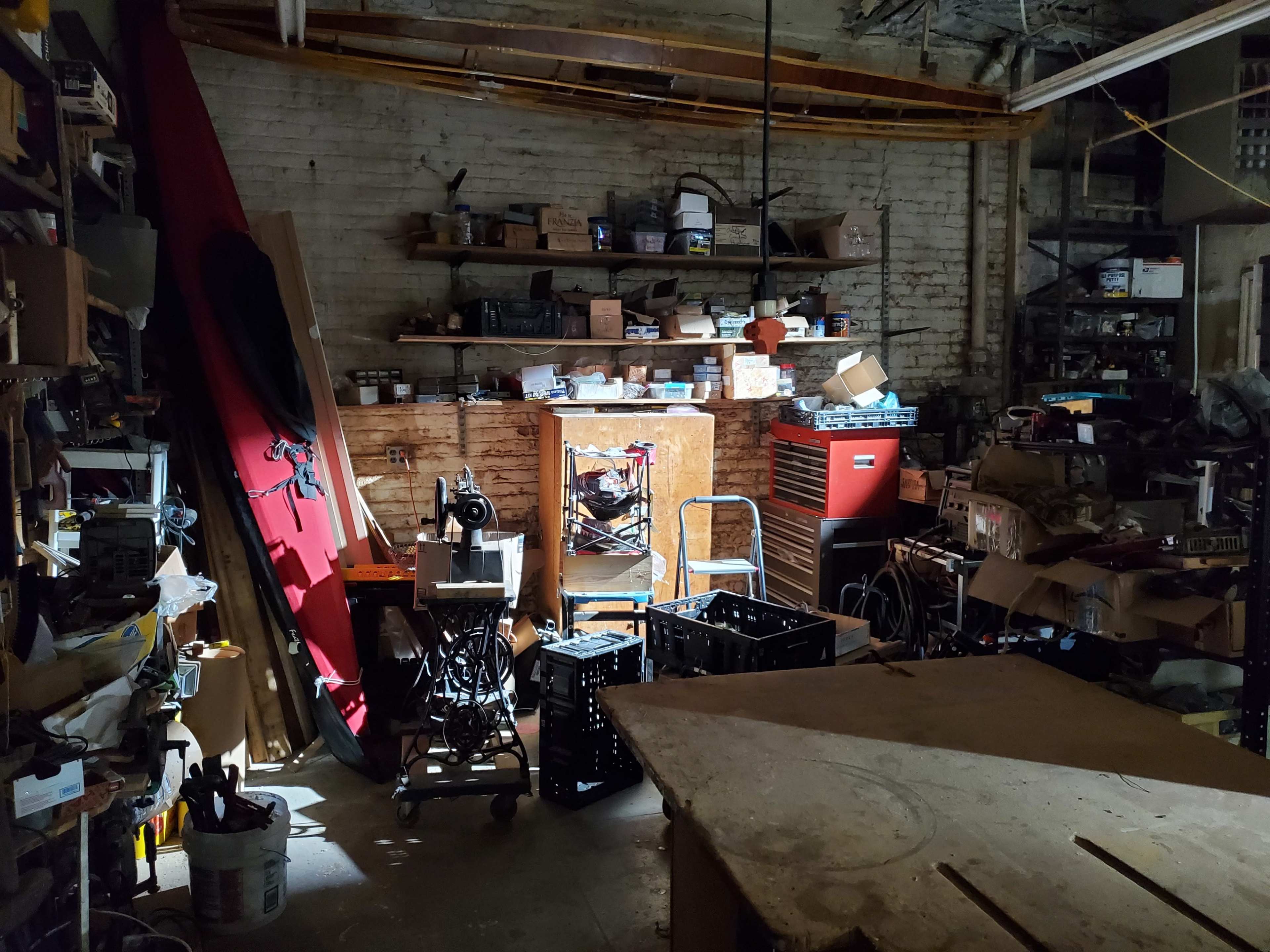 A dimly lit workshop filled with various tools, equipment, and boxes arranged throughout the space.