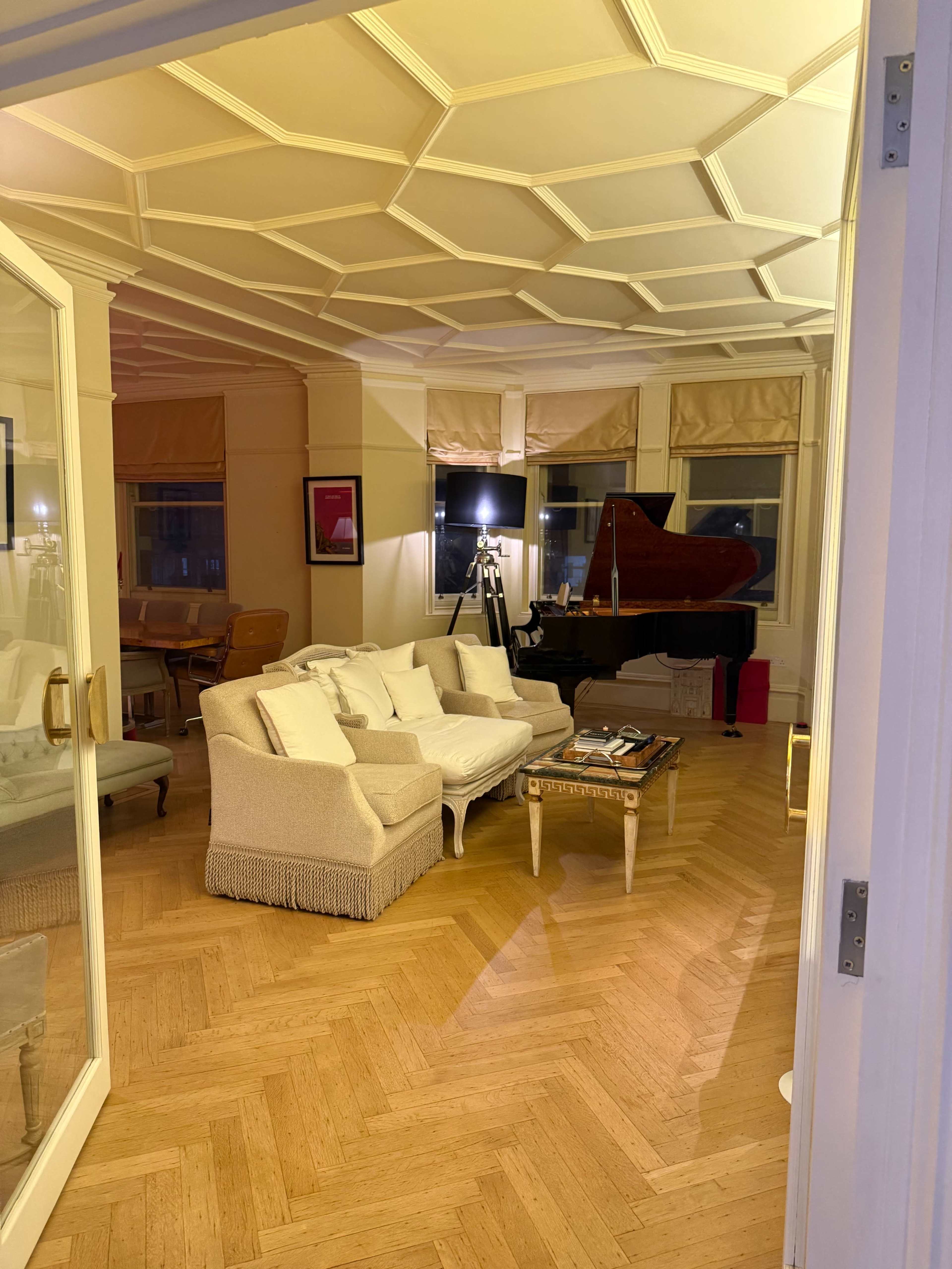 A cozy living room features a grand piano, a white sofa, and hardwood flooring, illuminated by soft lighting.