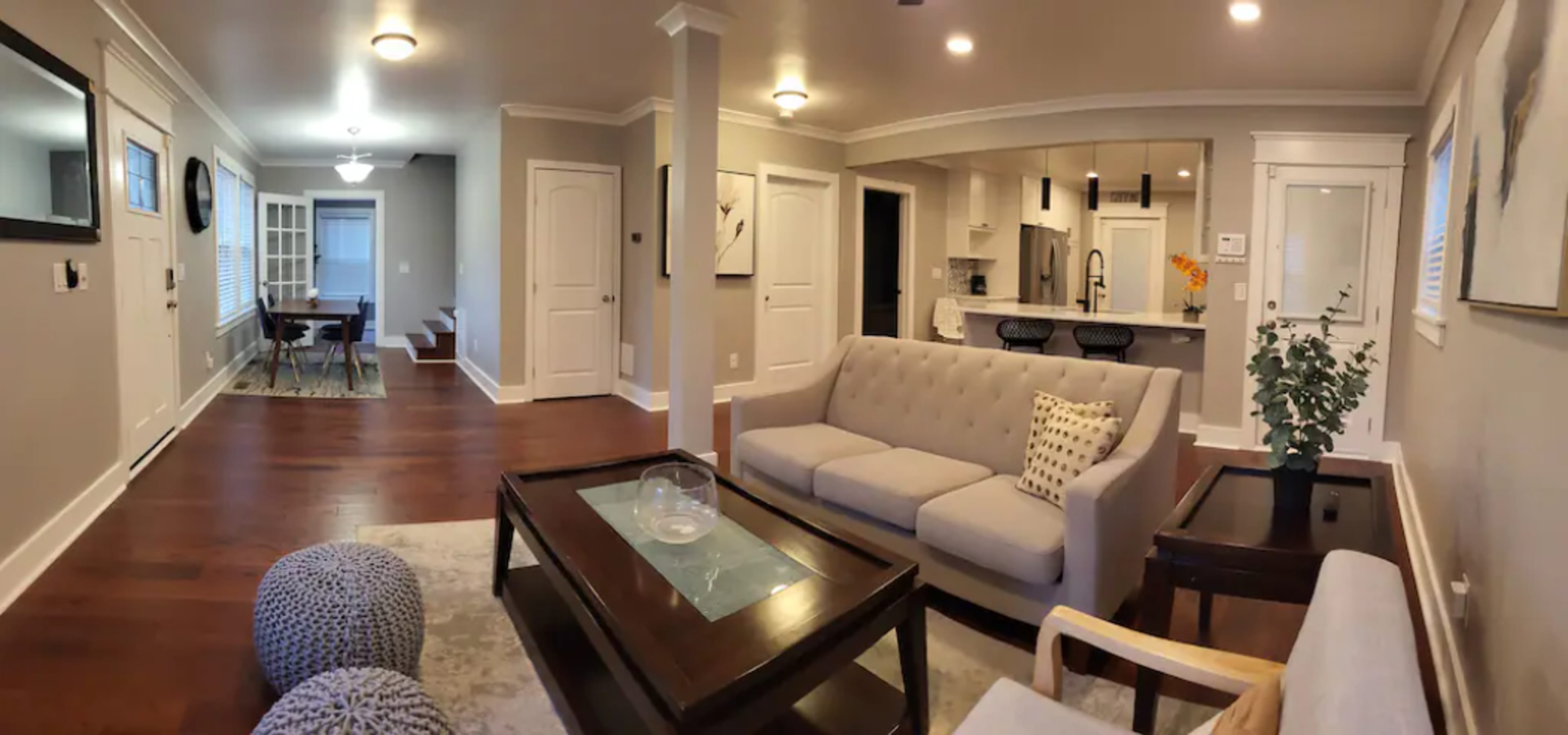 A spacious living room with a beige sofa, a coffee table, and a view into an adjacent dining area and kitchen.