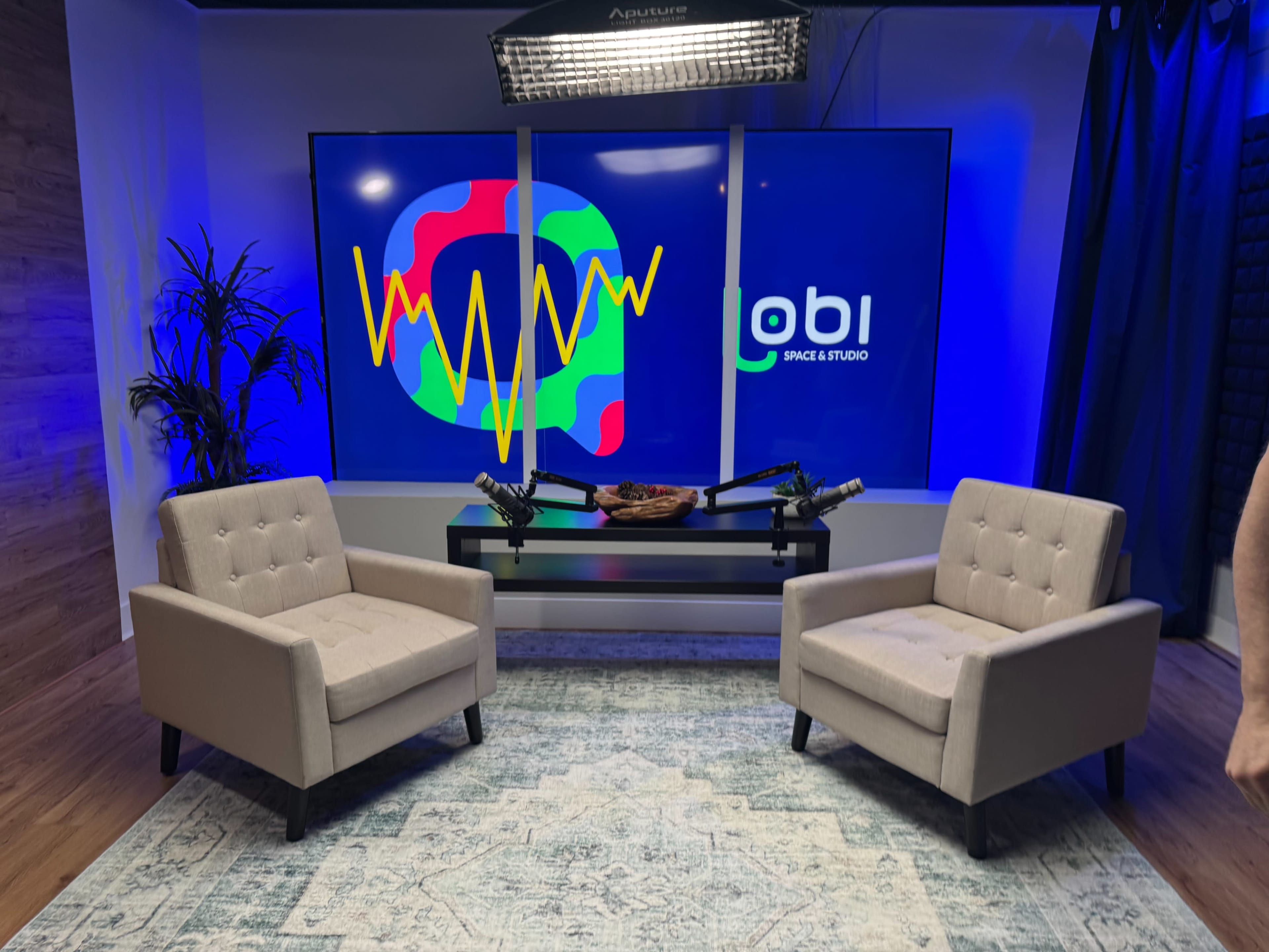 The image shows a modern studio setup with two light-colored chairs facing a digital screen displaying colorful abstract graphics and the logo for "obi Space & Studio."