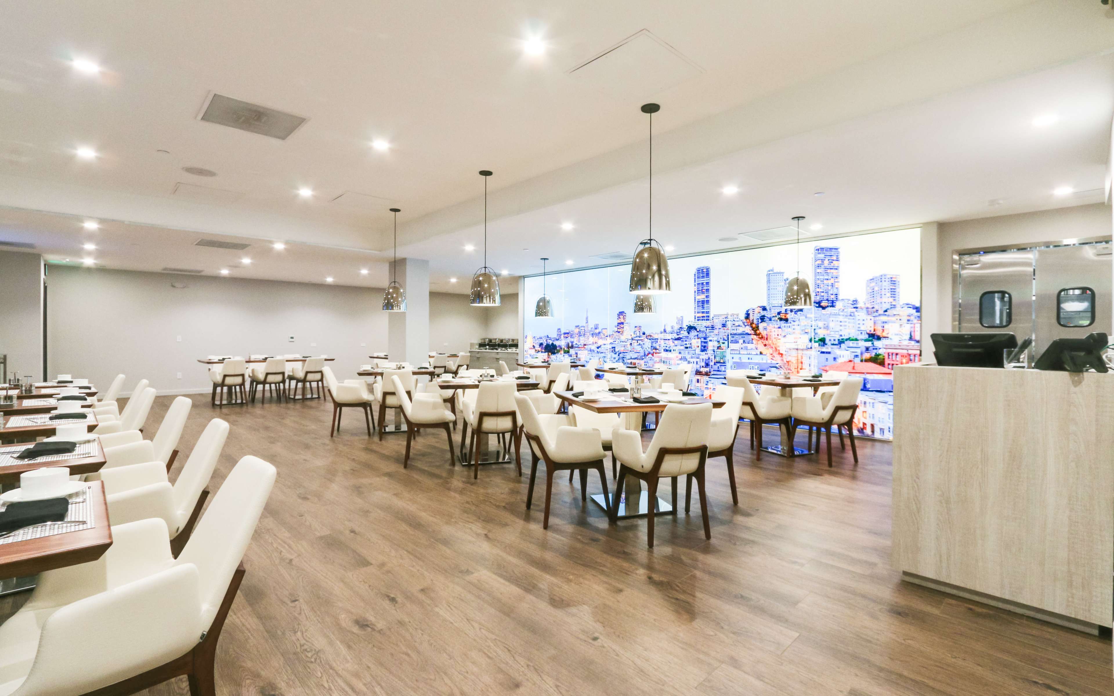 The image shows a modern restaurant interior with tables and chairs, illuminated by pendant lights, and featuring a large cityscape mural on one wall.