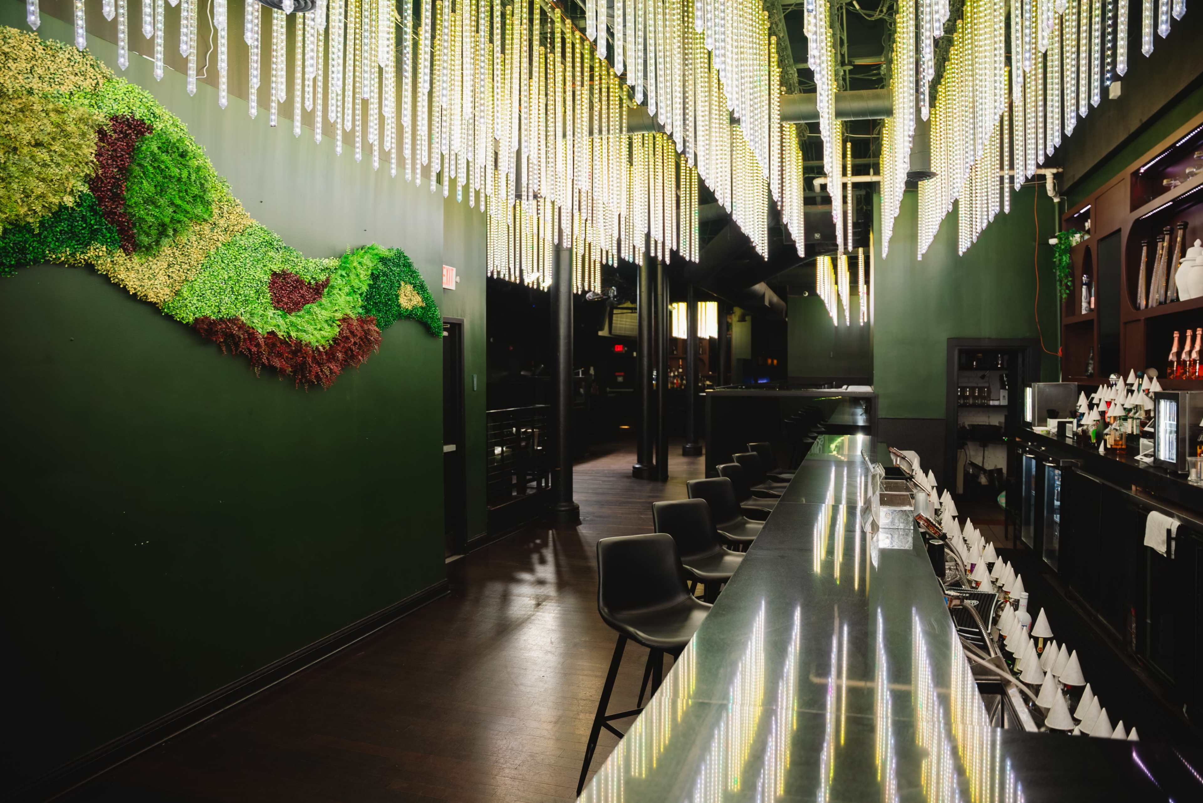 A sleek bar area features a long black countertop and vibrant green wall decor, illuminated by hanging light fixtures.