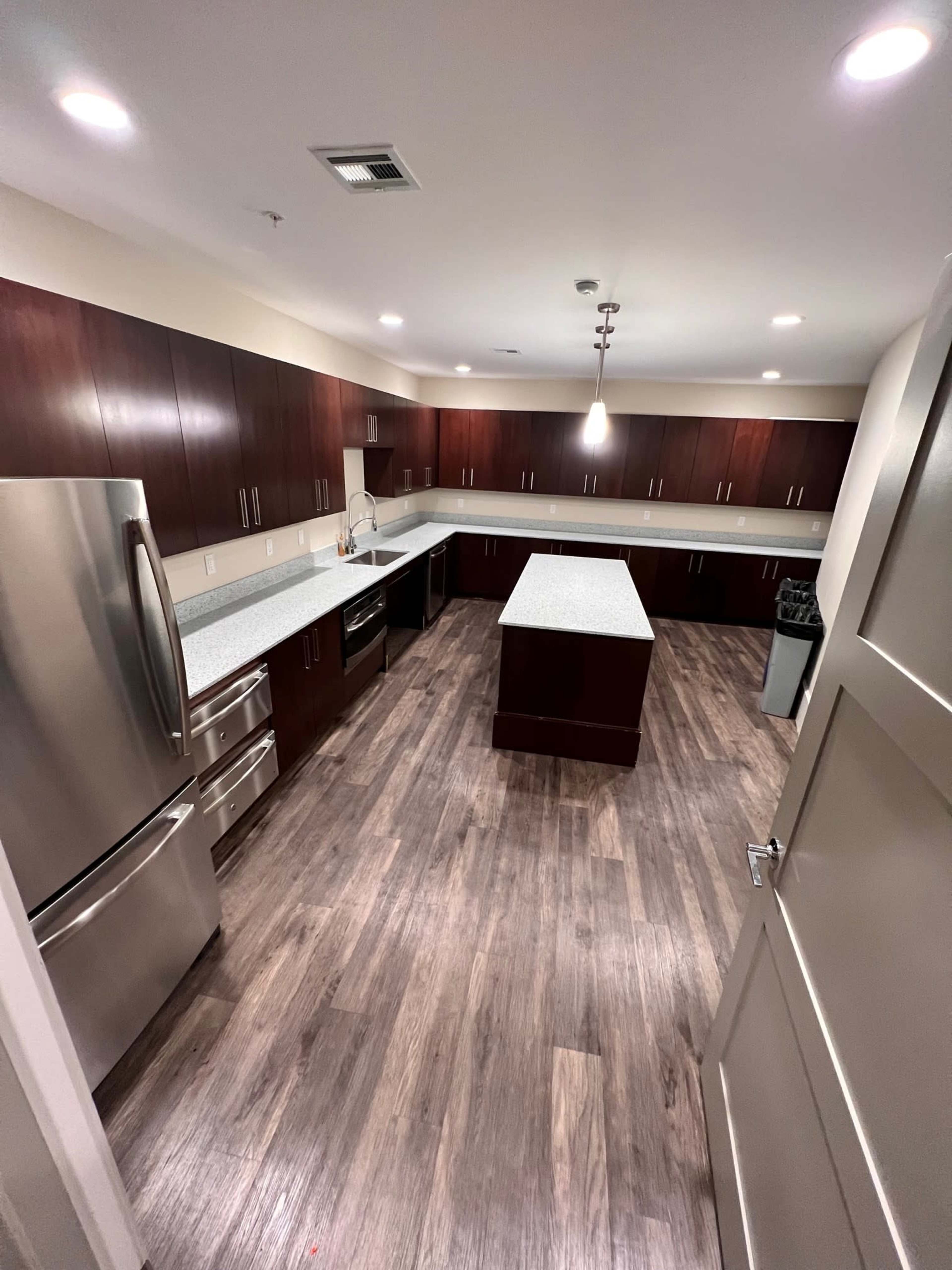 A modern kitchen with dark wood cabinetry, stainless steel appliances, and a large central island with a light-colored countertop.