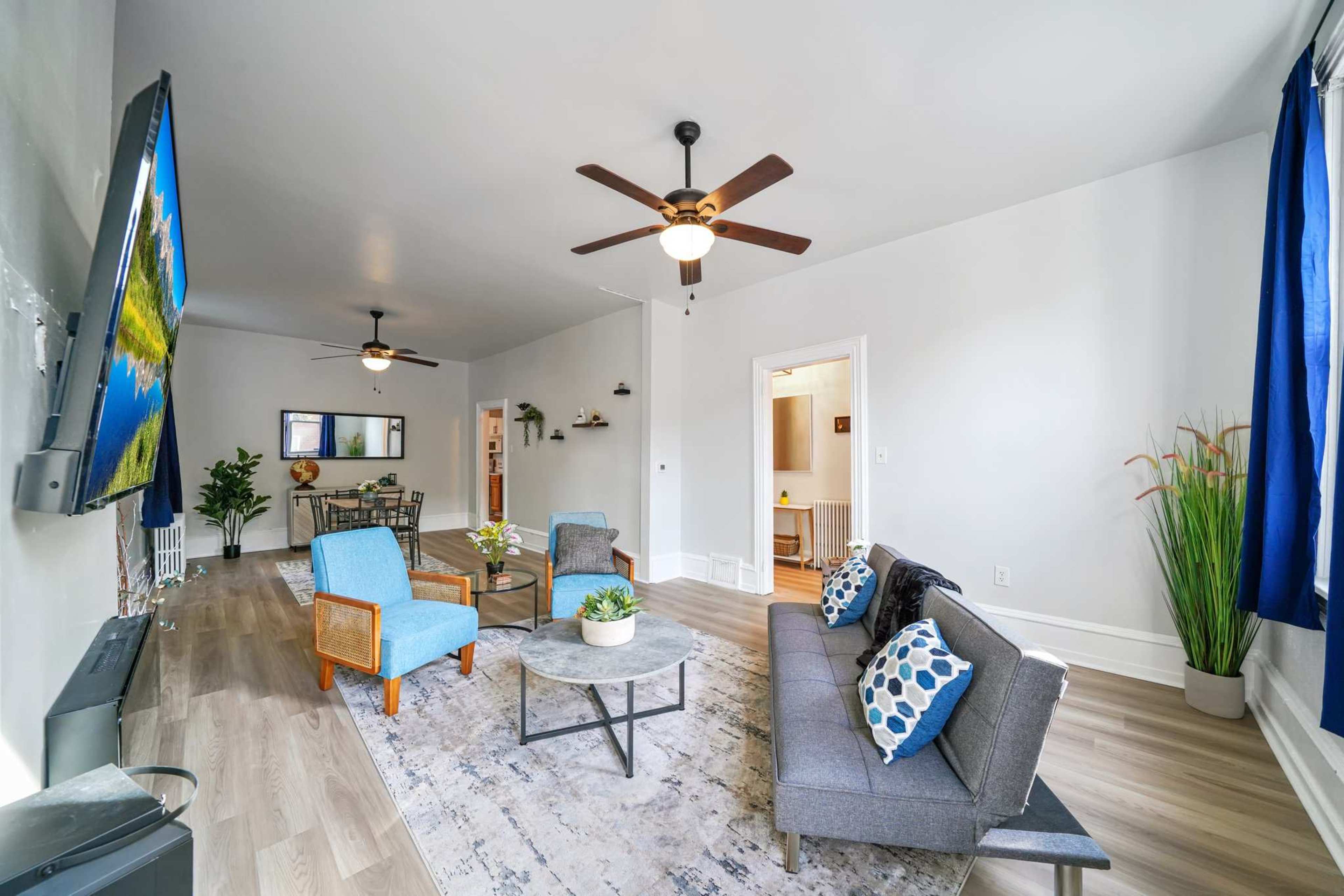 A spacious living room with two ceiling fans, modern furniture, and large windows allowing natural light.
