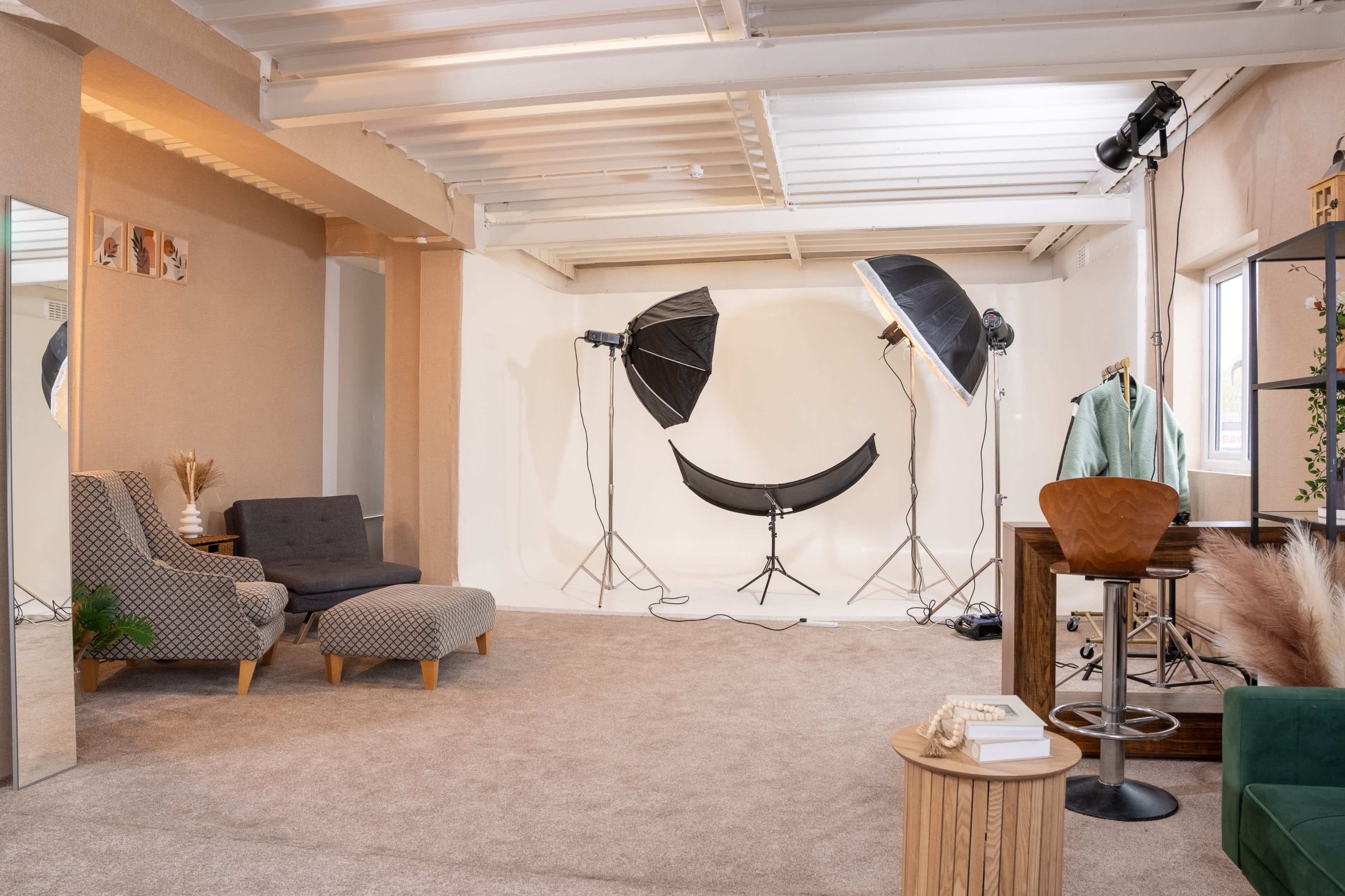 A spacious studio features a soft carpet, modern furniture, and professional lighting setups against a plain backdrop.
