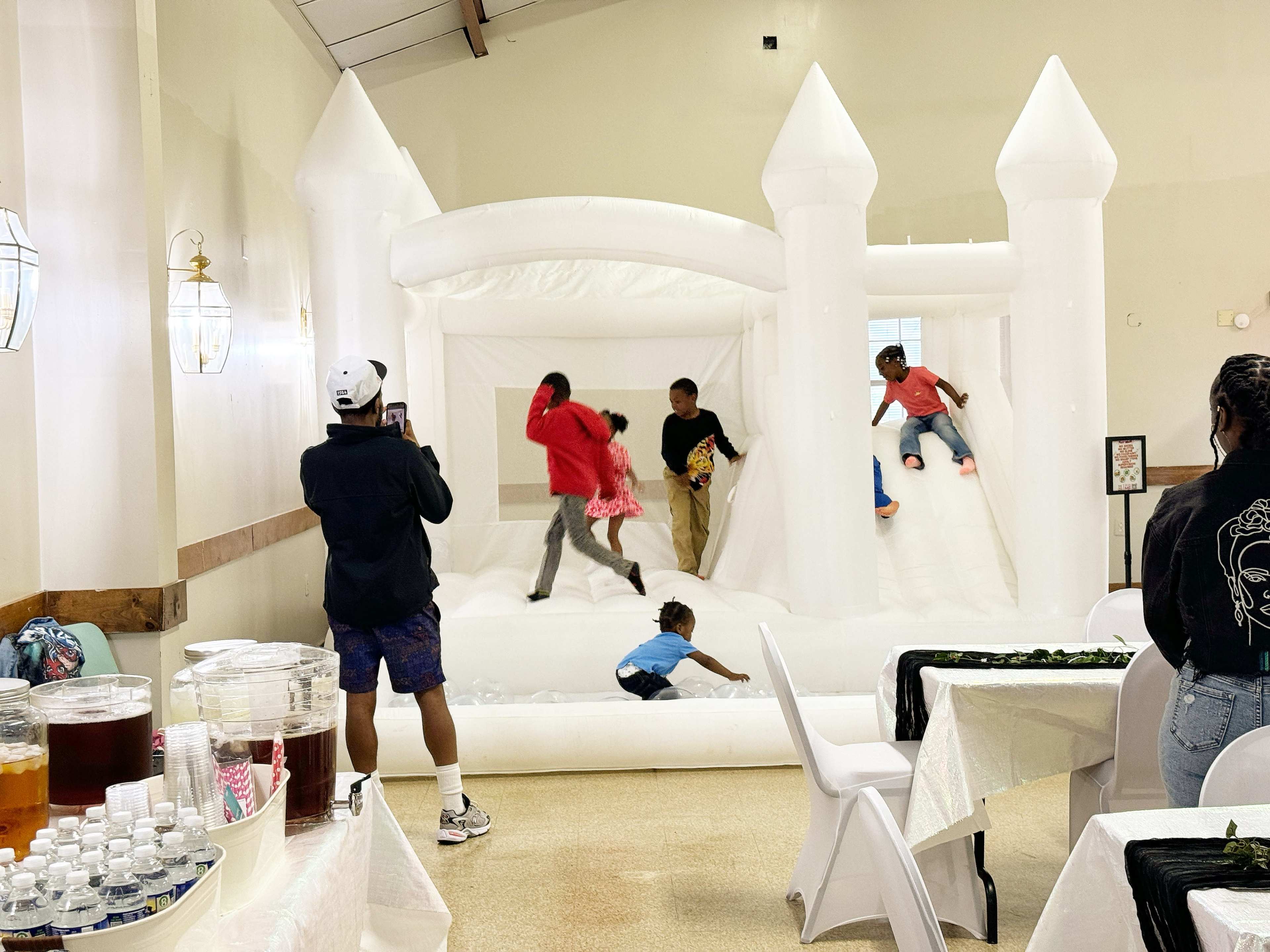 A group of children plays on an inflatable bounce house inside a decorated hall.