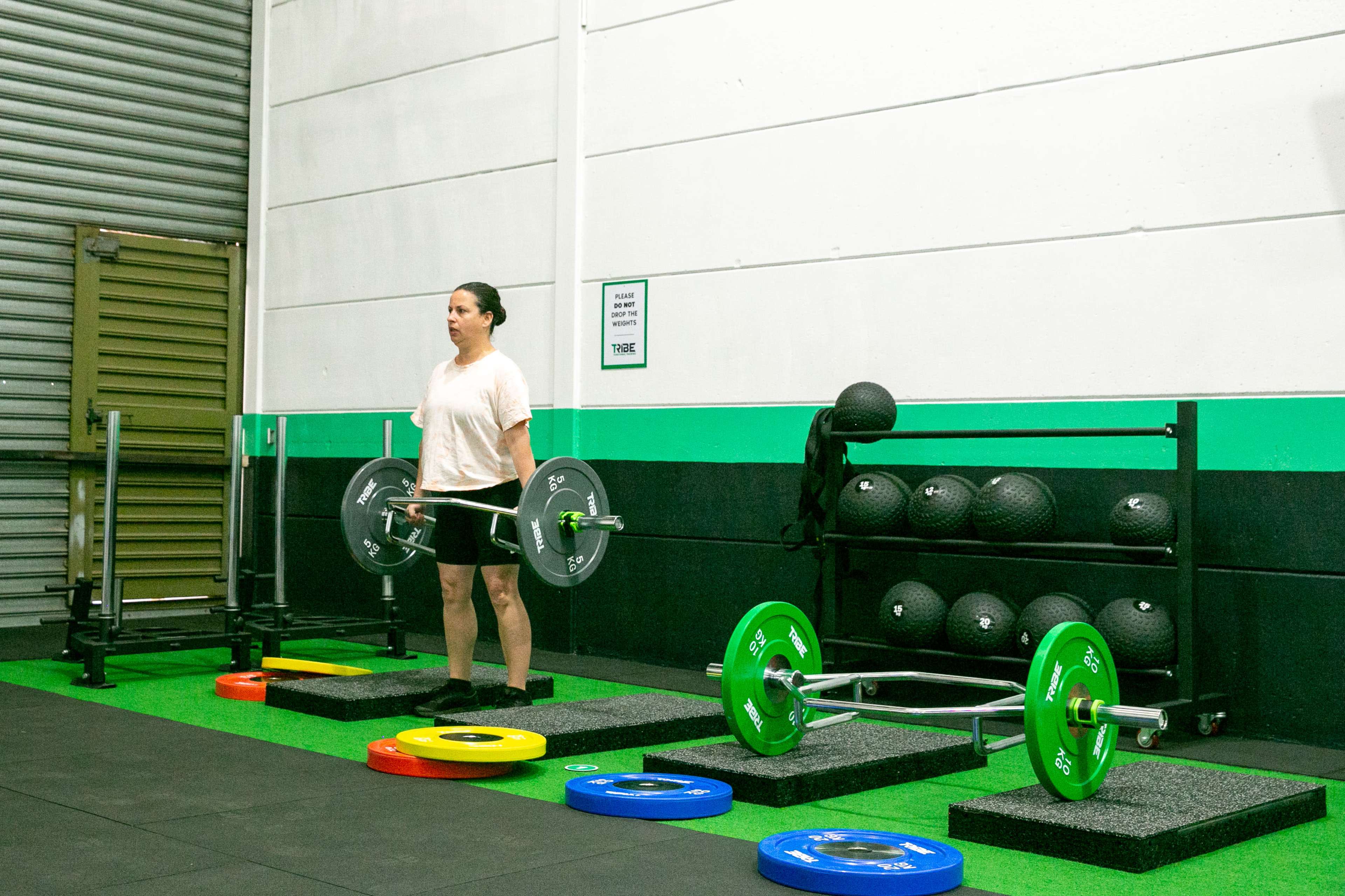 A person stands with a barbell in a gym, next to colorful weight plates and fitness equipment.