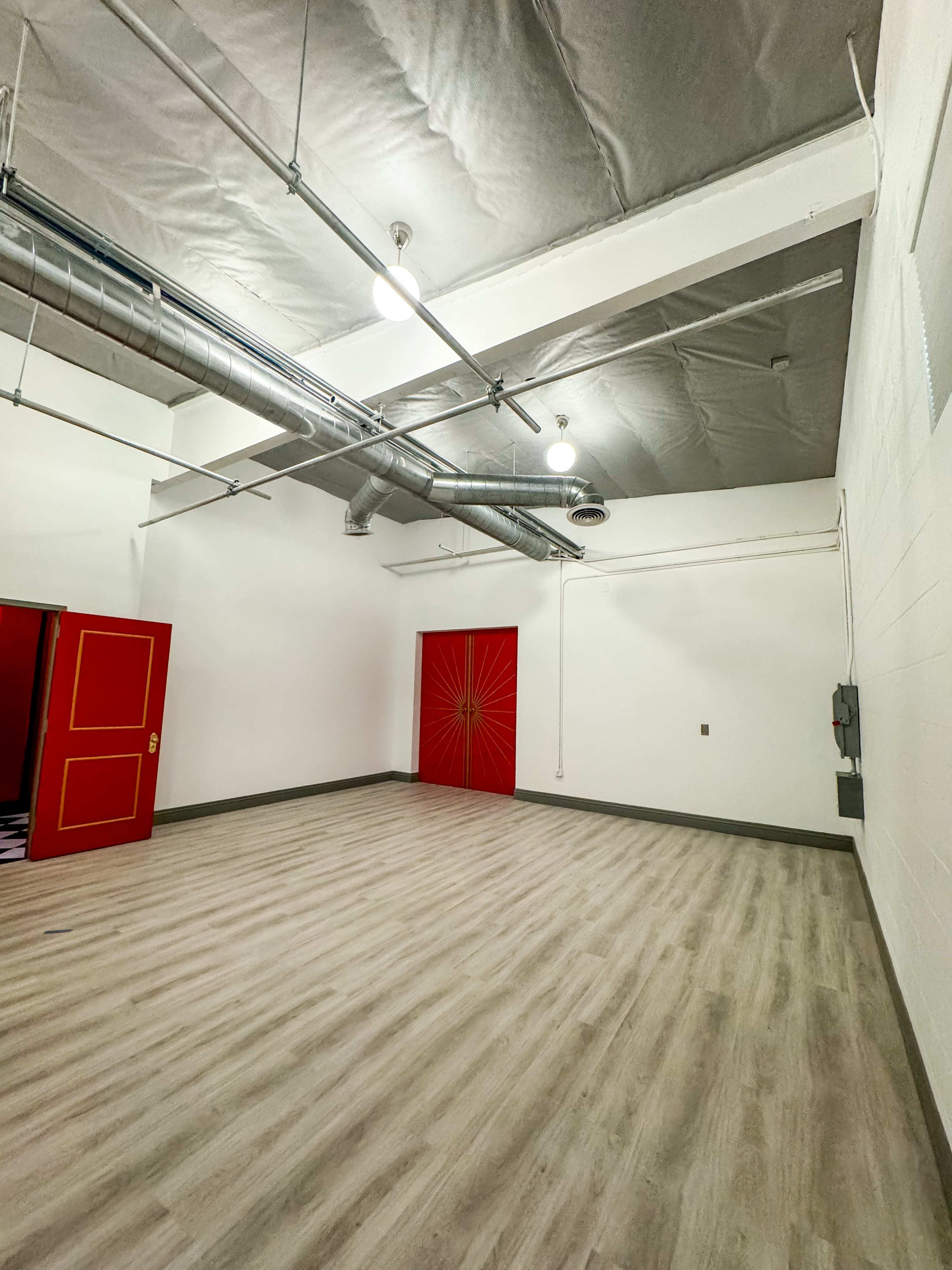 An empty room with a wooden floor, white walls, and a red door featuring a sunburst design.