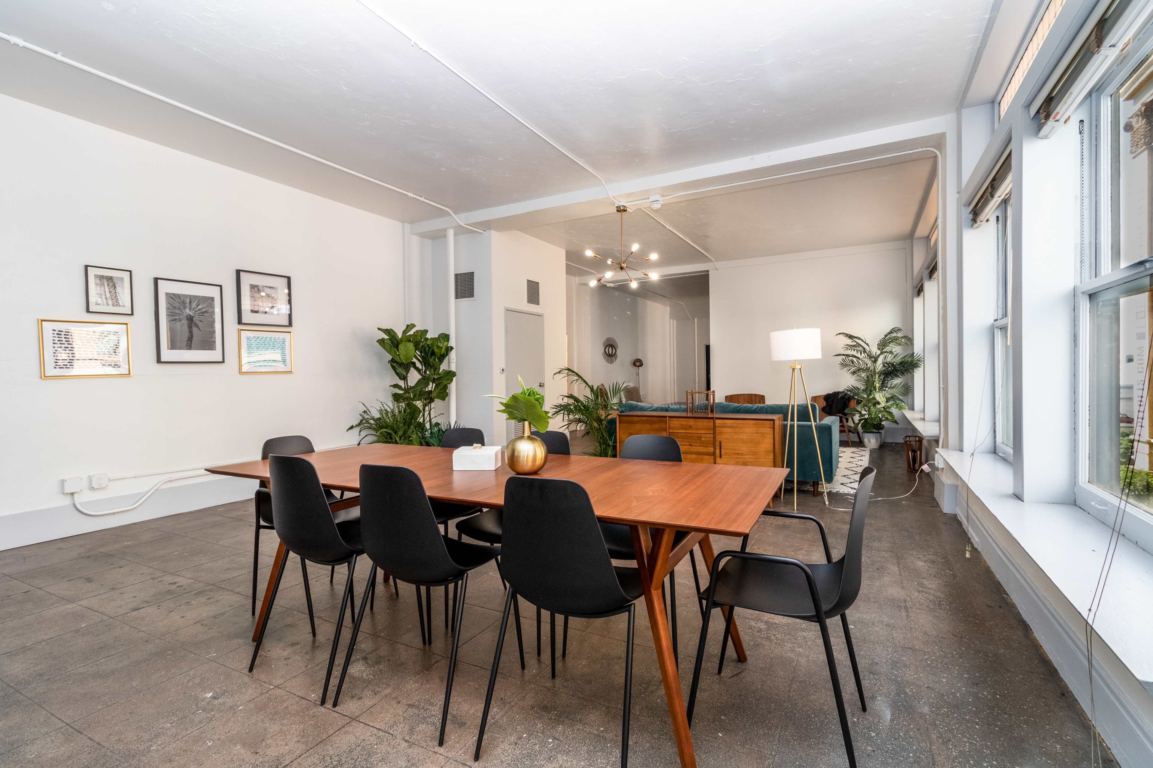 A modern dining area features a wooden table surrounded by black chairs, with plants and artwork adorning the white walls.