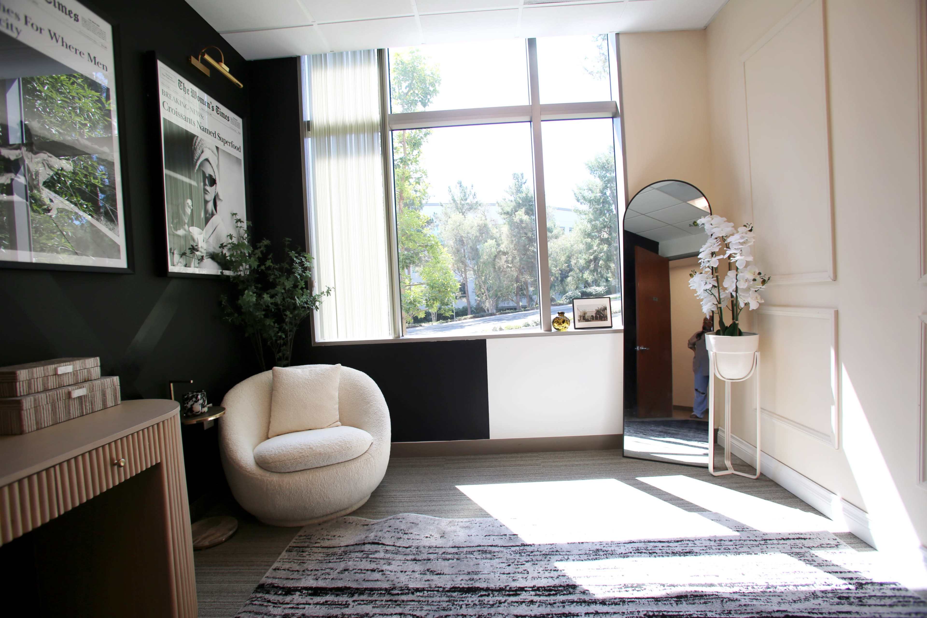 The image depicts a modern room featuring a round, white chair, a large window with natural light pouring in, a full-length mirror, and decorative plants, set against a backdrop of contrasting black and white walls.