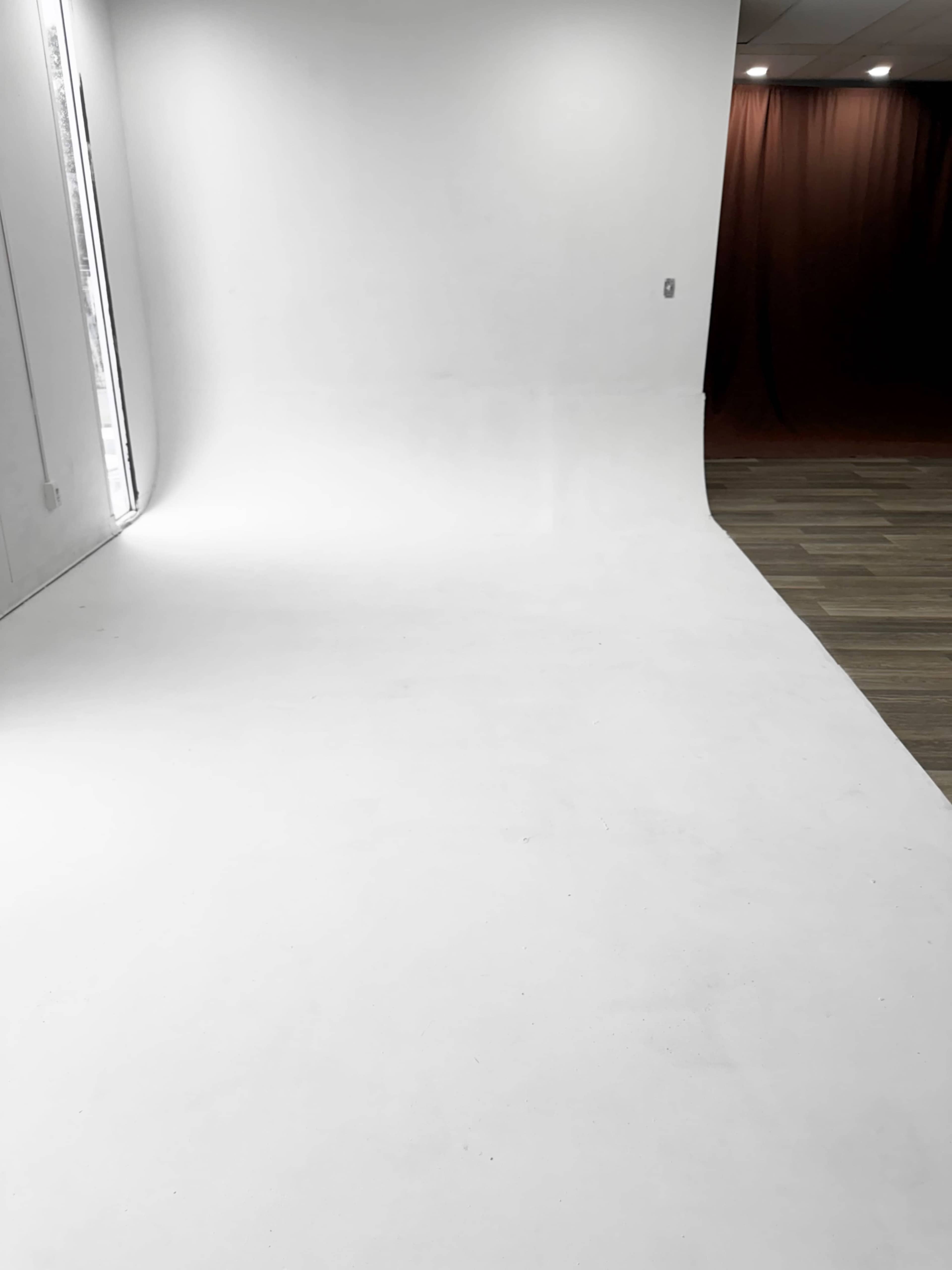 The image shows a spacious photo studio with a white curved backdrop and wooden flooring.