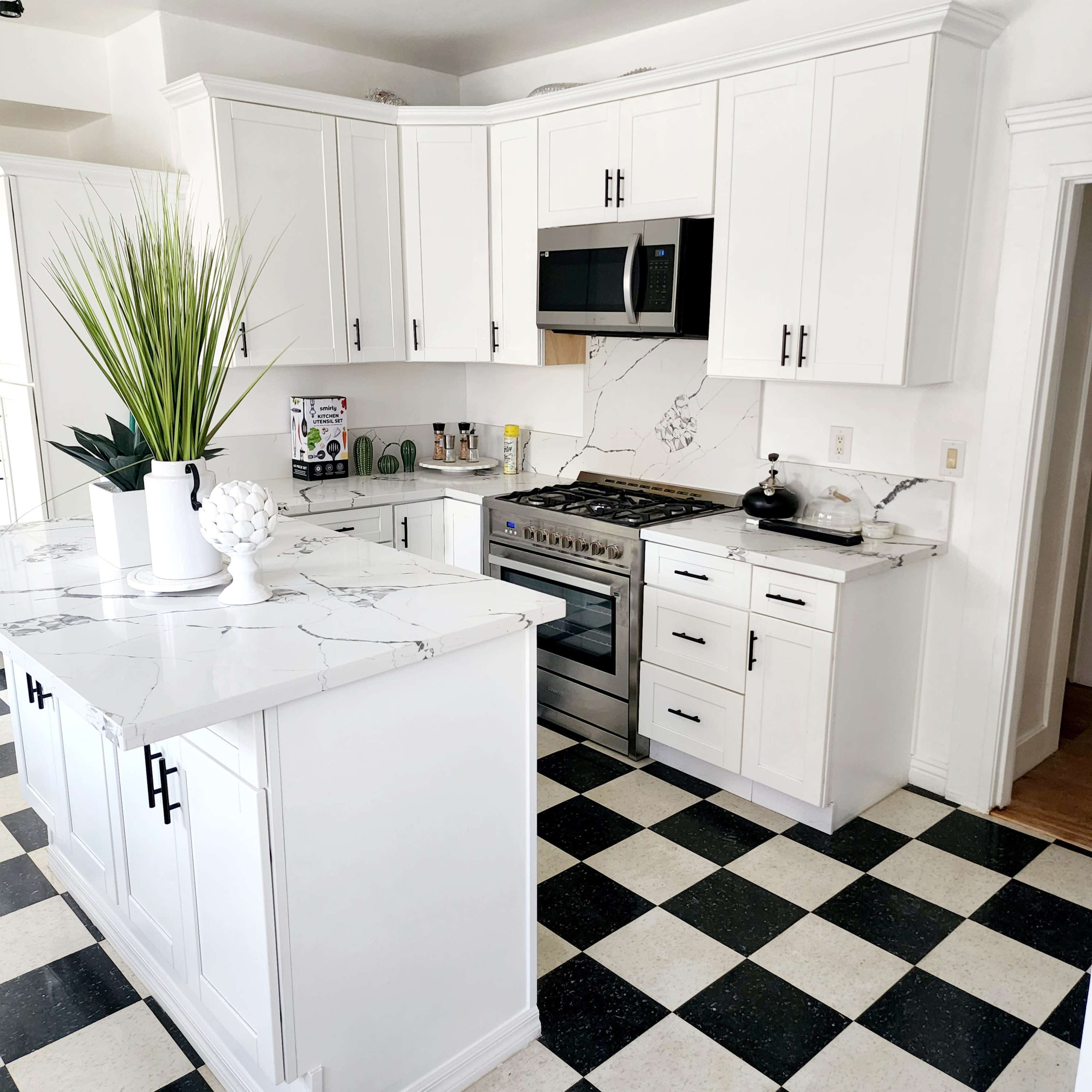 A modern kitchen featuring white cabinets, a marble countertop, and a checkered black-and-white floor.