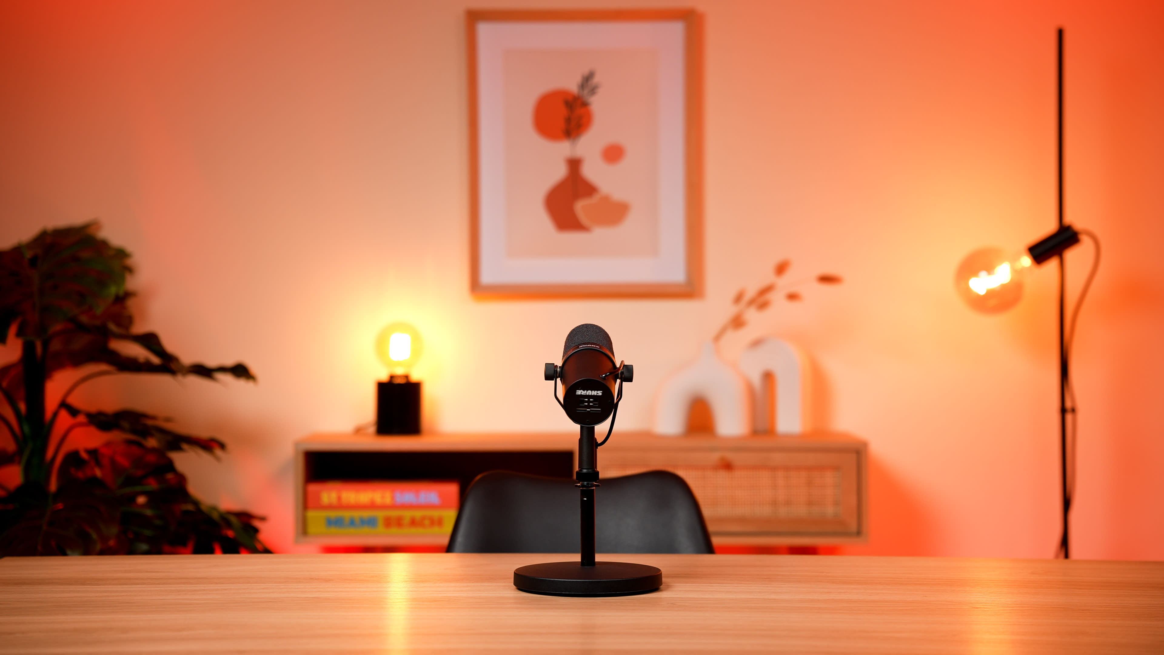 A microphone is positioned on a wooden table in a well-lit room adorned with modern artwork and decorative elements.
