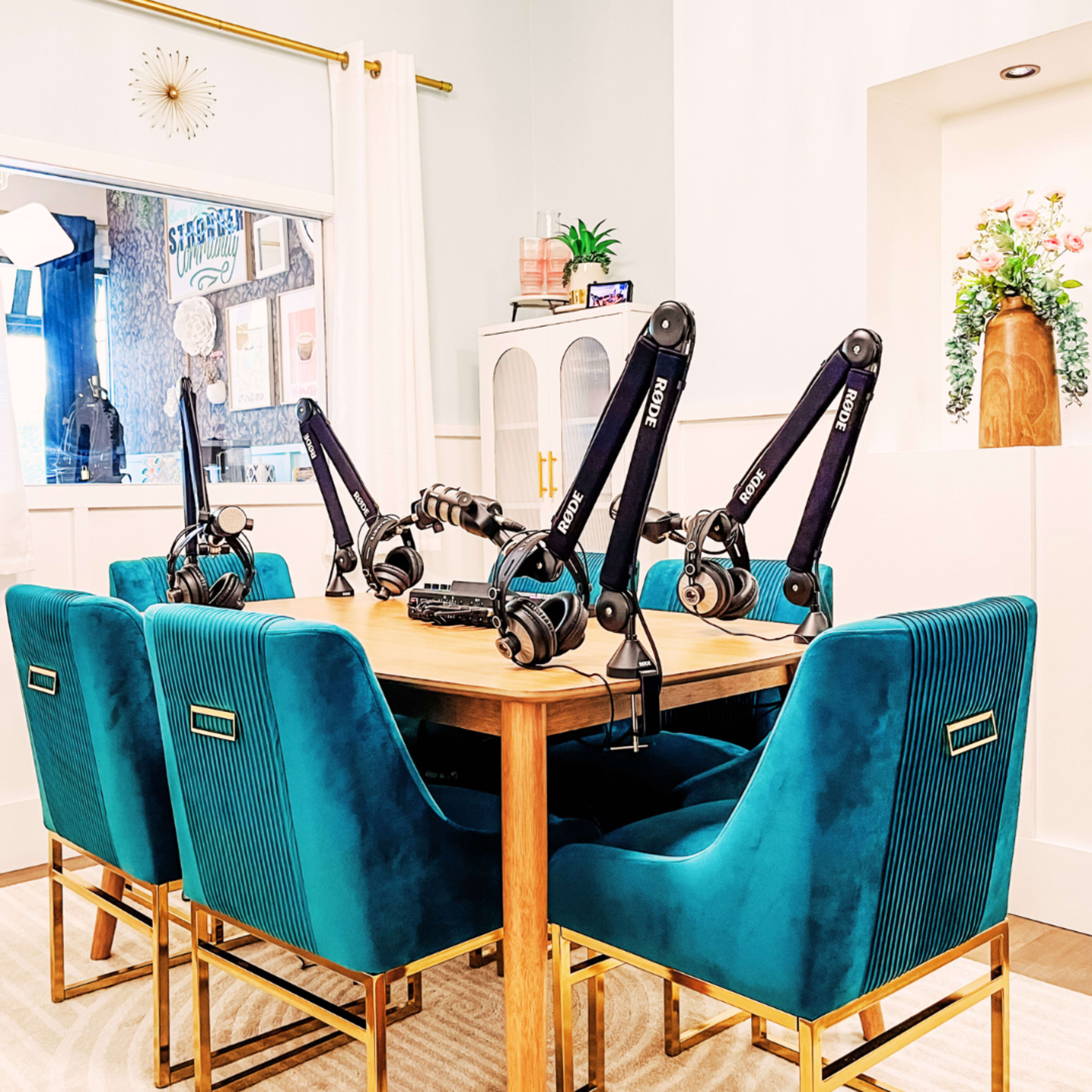 The image shows a modern dining table surrounded by six teal velvet chairs, each equipped with a microphone arm and headphones, set in a bright room with plants and decorative elements.