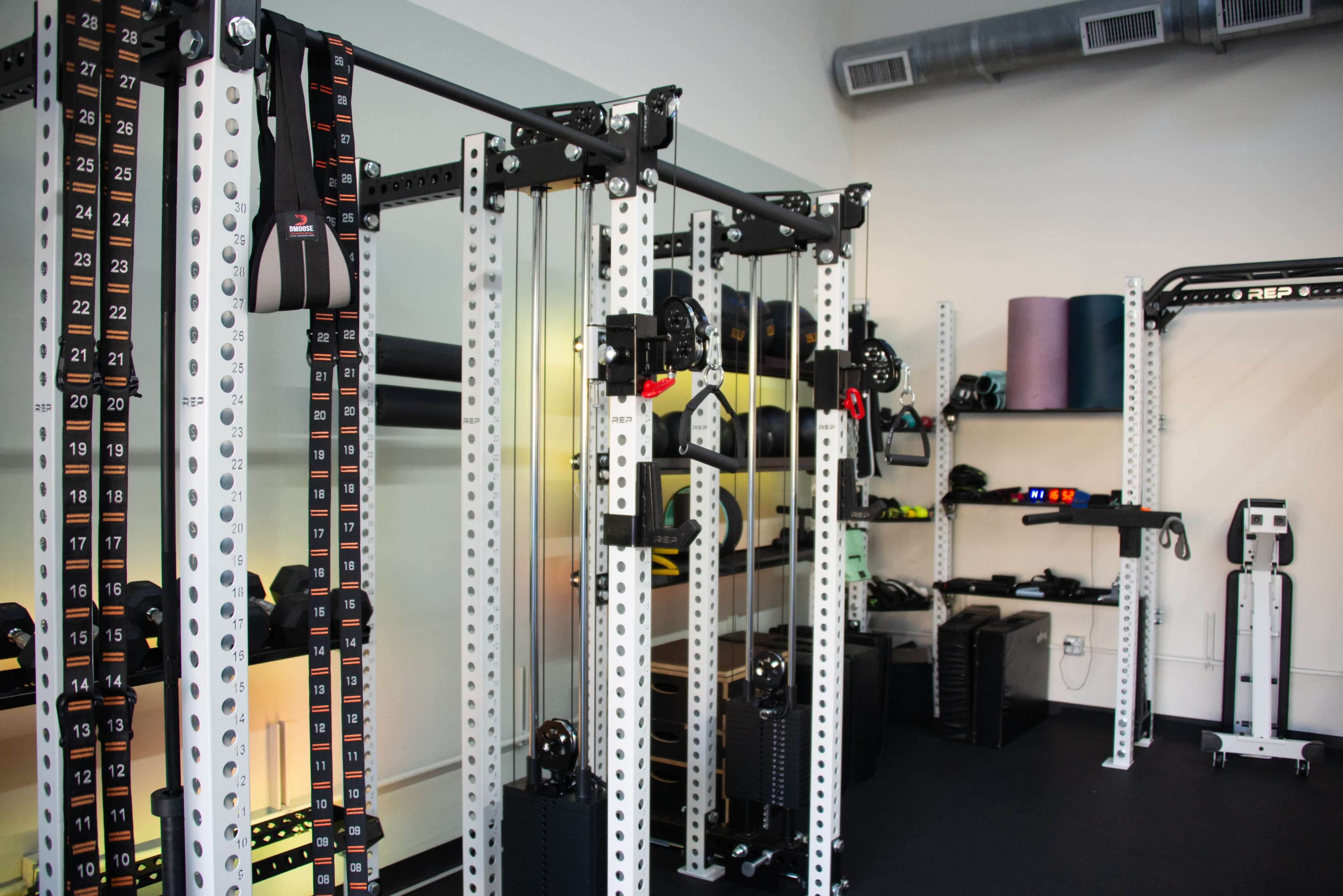 The image shows a well-equipped gym featuring multiple resistance machines and free weights organized in a clean, modern space.