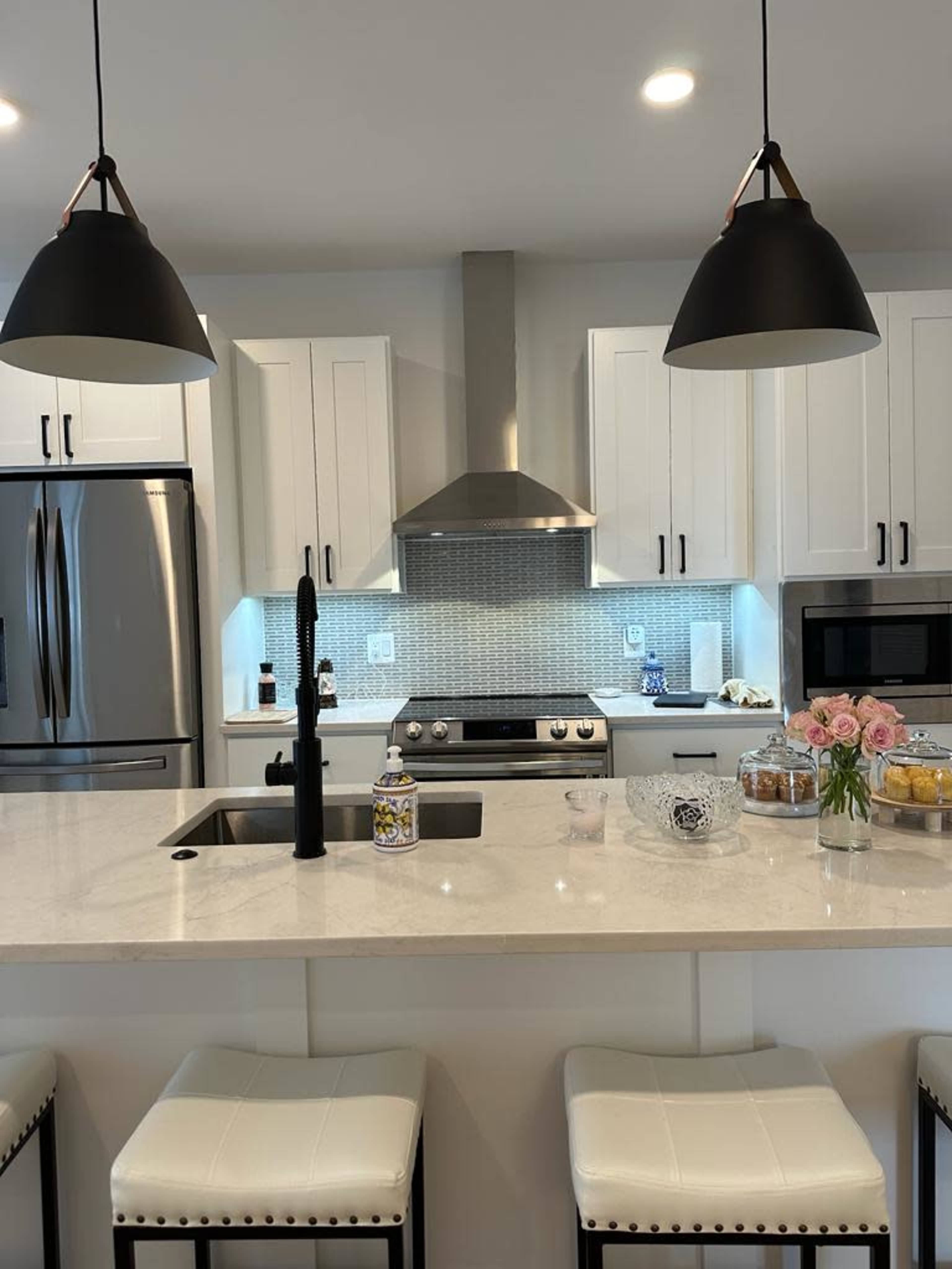 A modern kitchen features white cabinets, stainless steel appliances, a stone countertop, and a central island with bar stools.